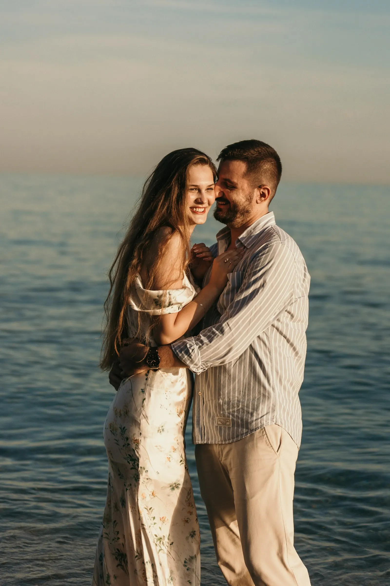 La pareja, mejilla con mejilla y sonriendo, de pie en el mar en calma, en la playa de Nerja