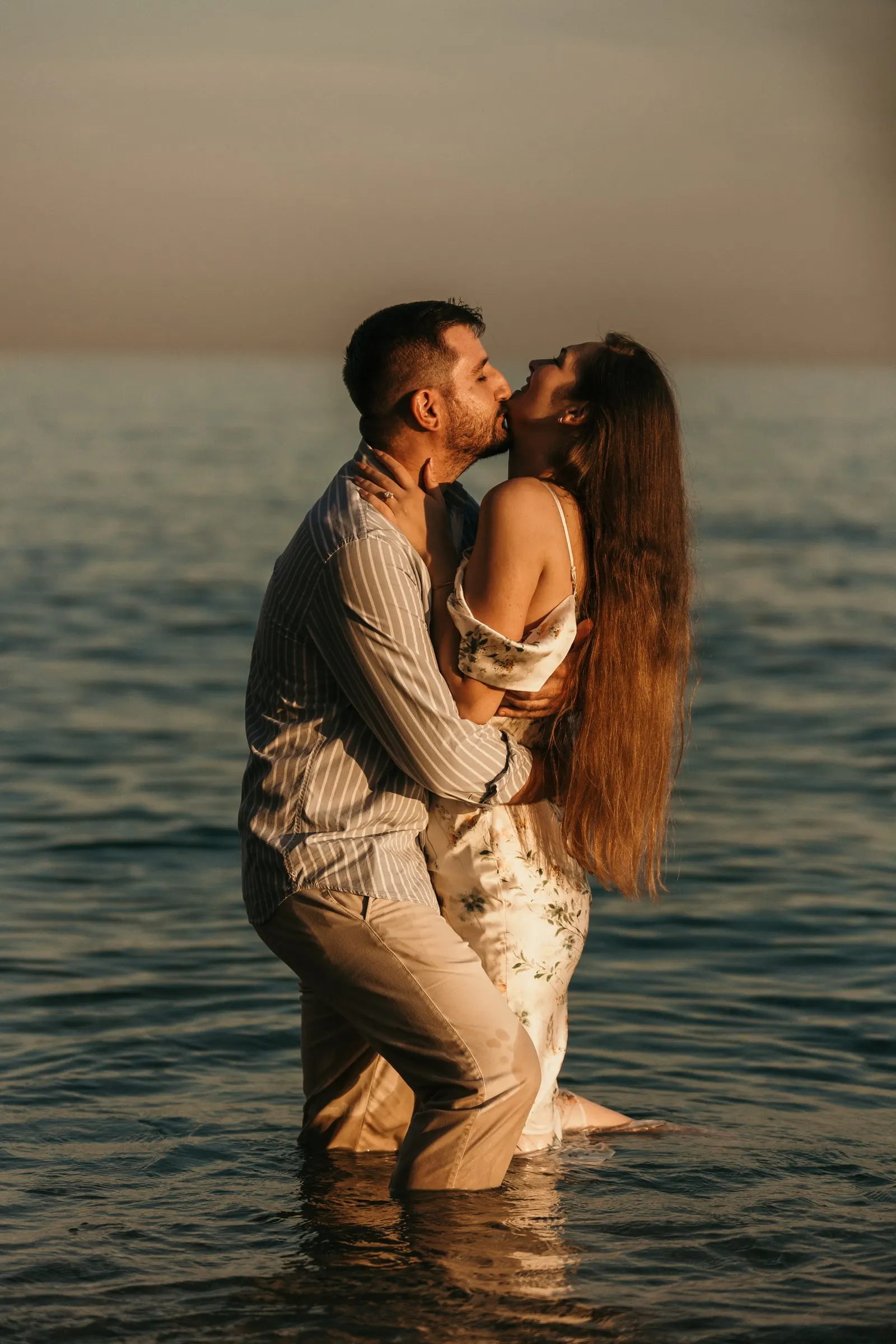 La pareja se besa con el agua por la cintura bajo una luz ámbar, en la playa de Nerja