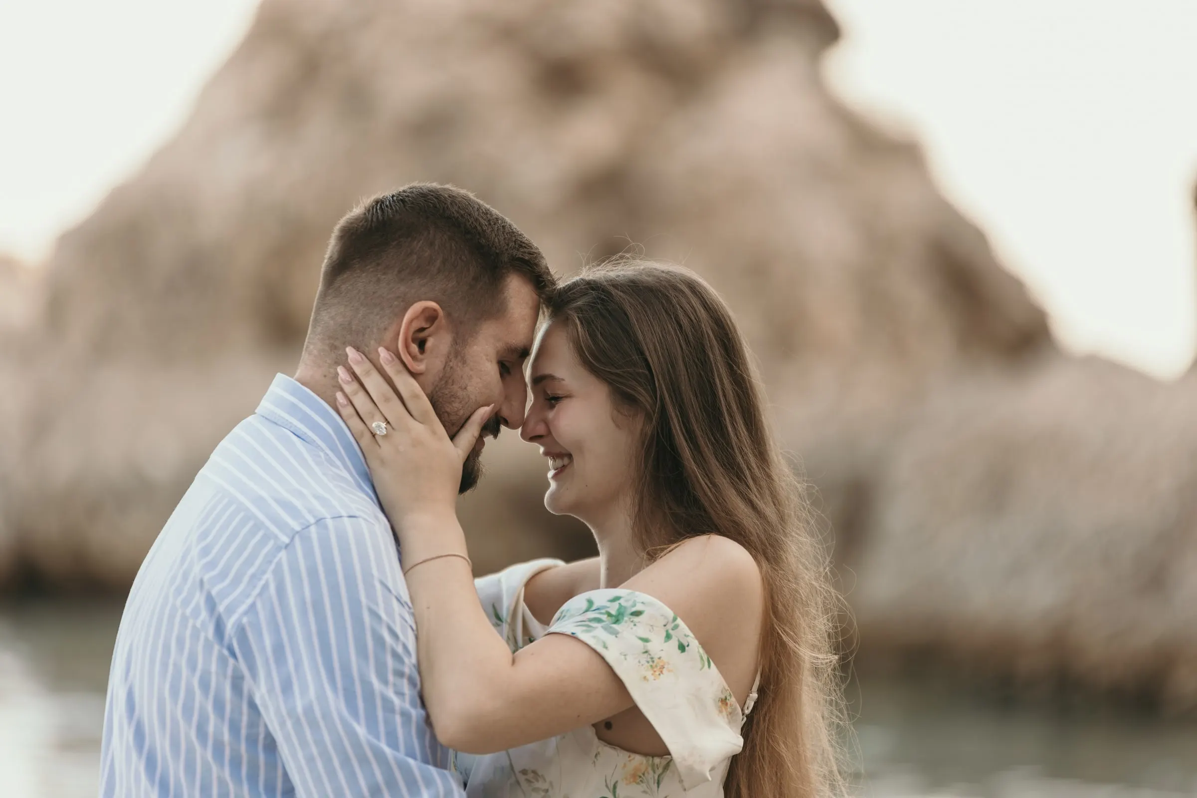 La pareja frente con frente, con el anillo a la vista y las rocas detrás, playa de Nerja
