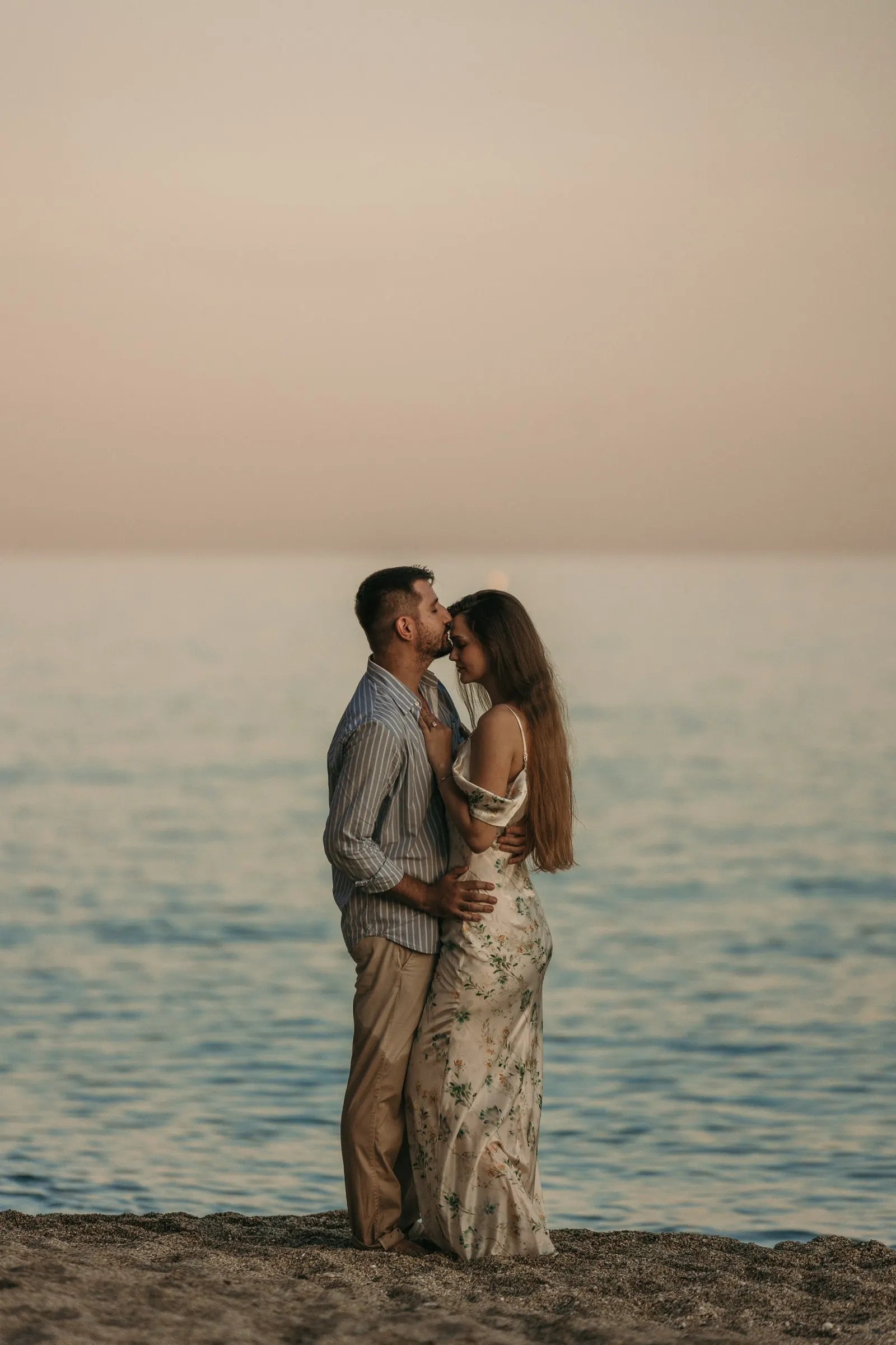 Couple kissing on the shore against a pink evening sky on the beach in Nerja