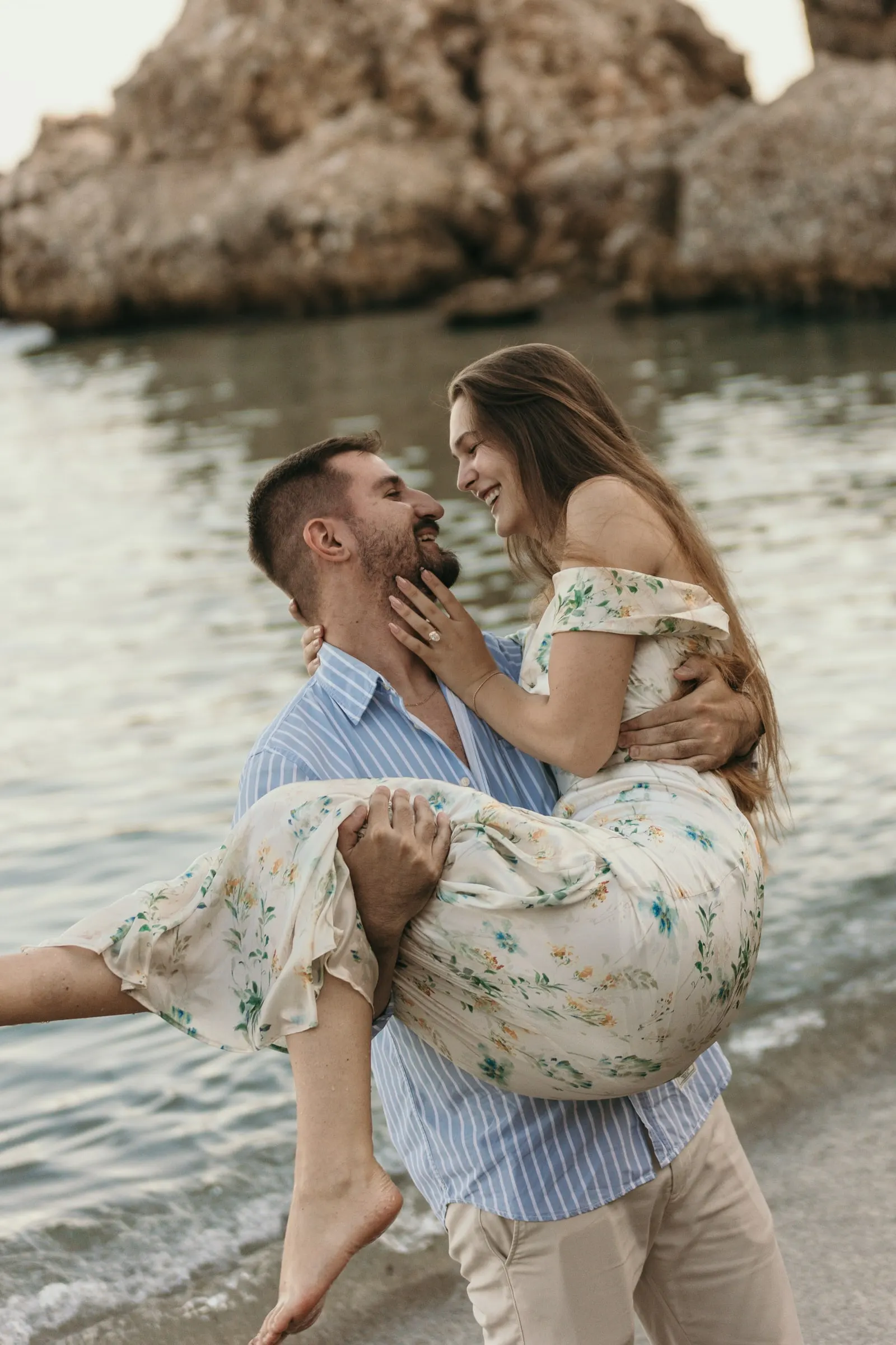 He lifts her in his arms beside the rocks as she smiles down at him, on the beach in Nerja
