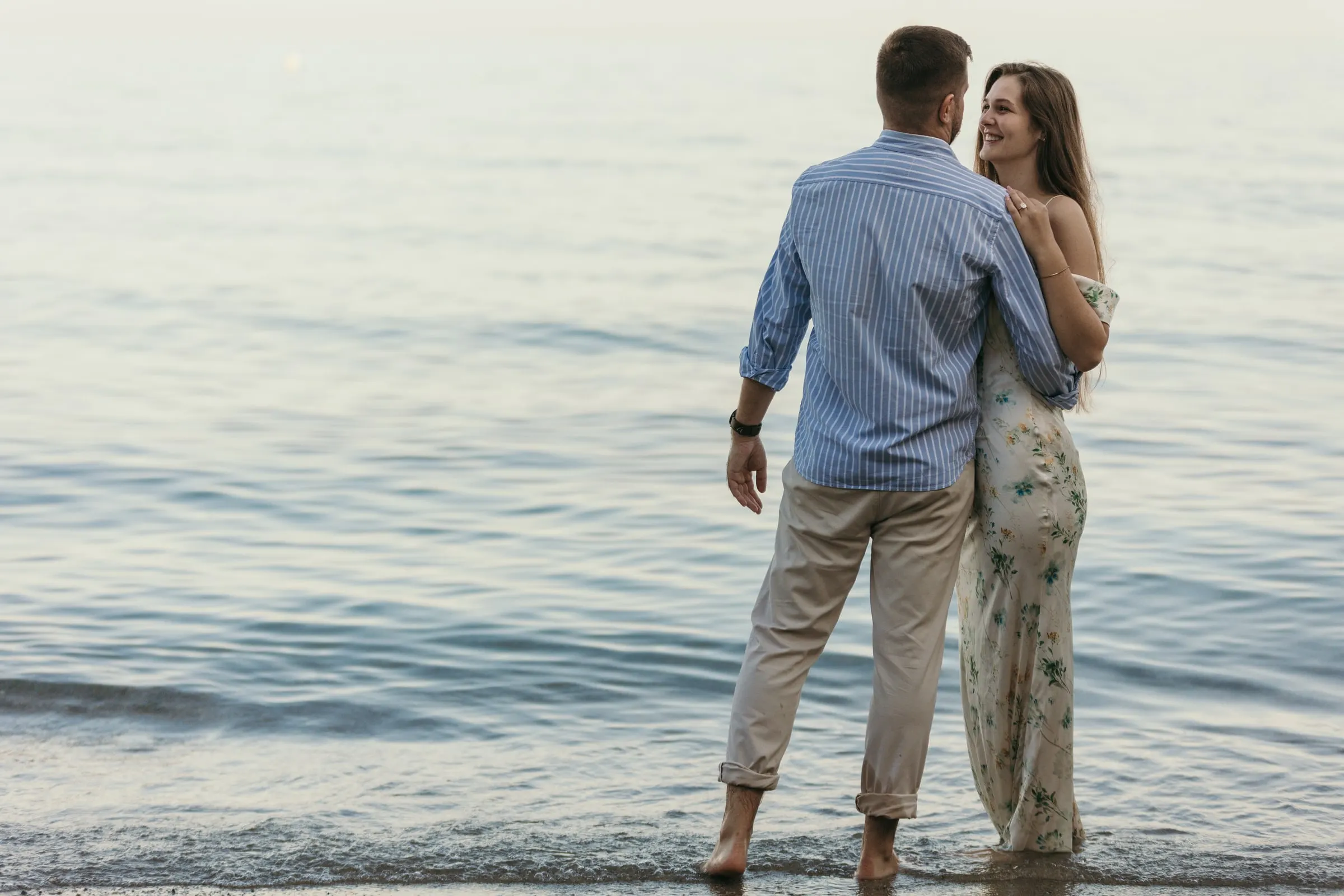 La pareja de pie en el agua mientras ella se gira sonriendo, en la playa de Nerja