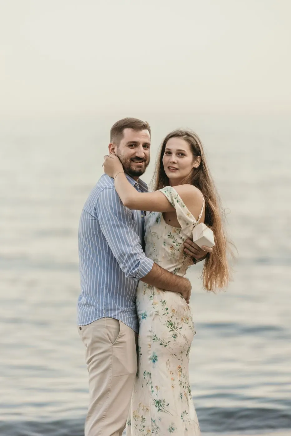 La pareja abrazada mirando a cámara, con el mar en calma detrás, en la playa de Nerja