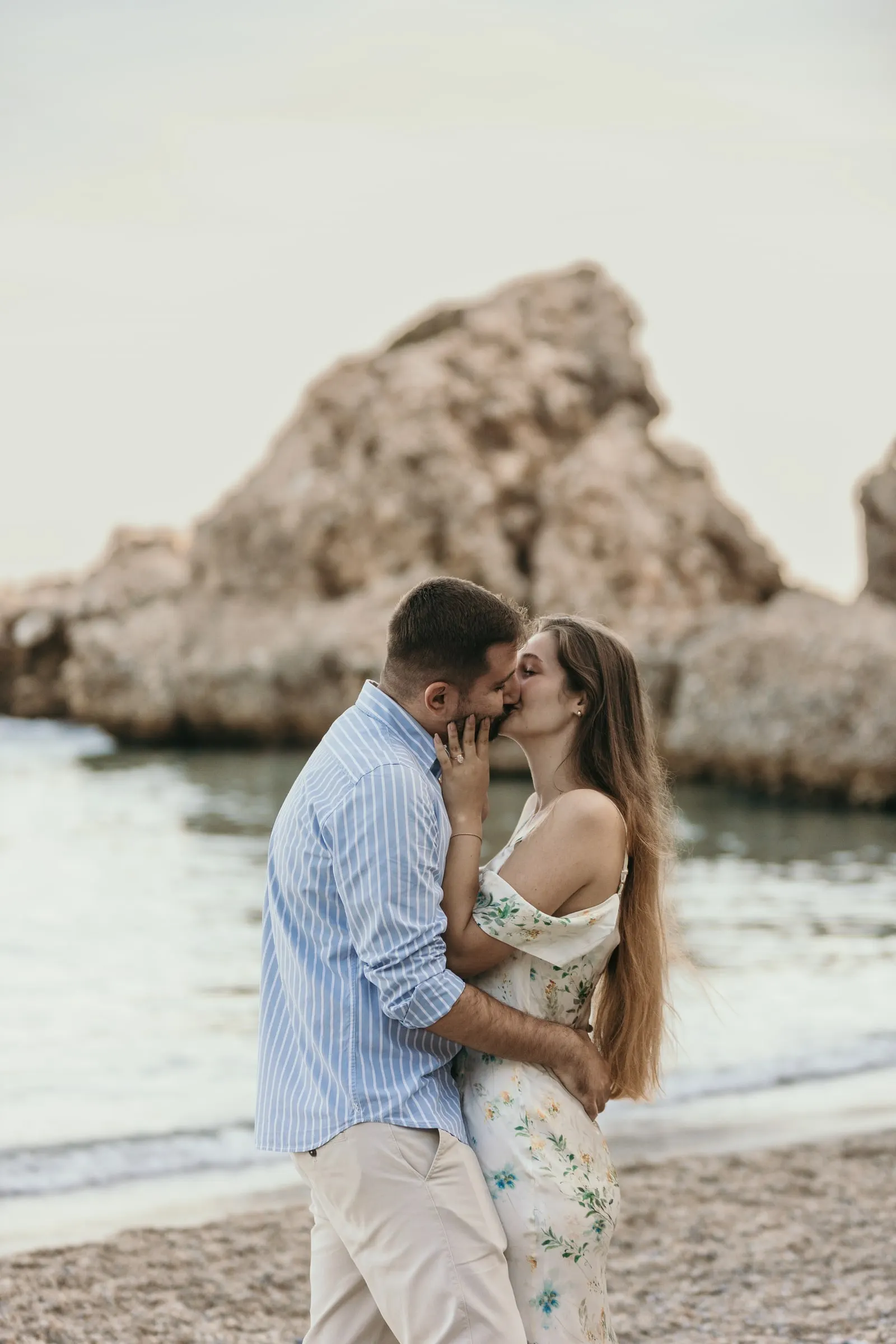 La pareja se besa sobre la grava con una gran roca en el mar detrás, en la playa de Nerja