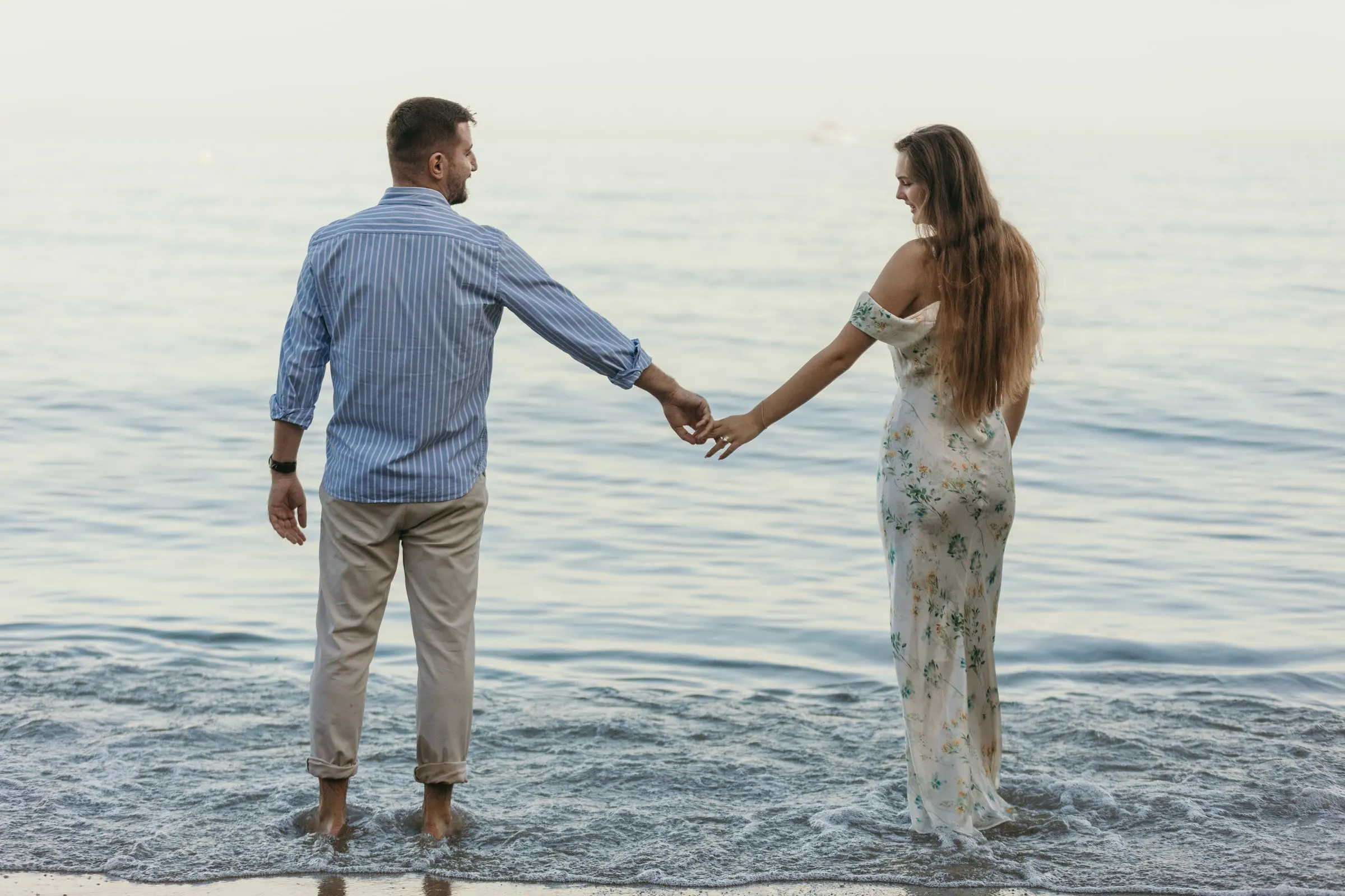 La pareja se da la mano mientras entra en el mar, en la playa de Nerja