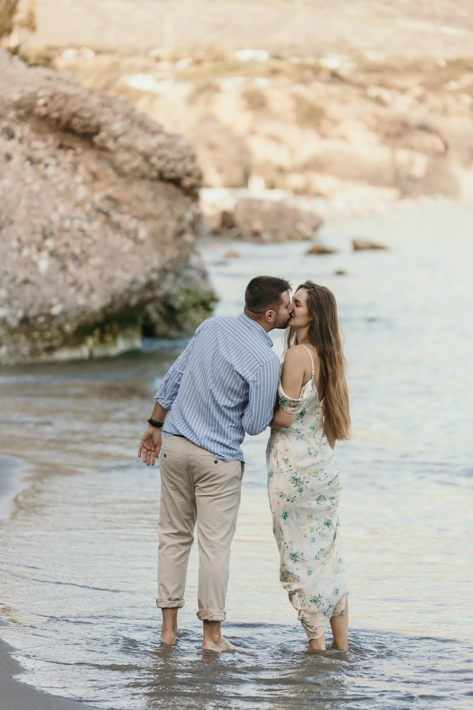 Él la besa mientras están descalzos en el agua bajo las rocas, en la playa de Nerja