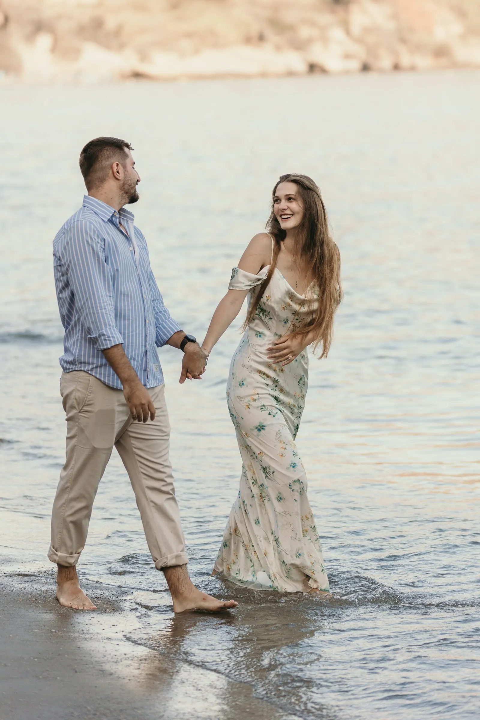 La pareja ríe mientras camina de la mano por el agua de la orilla, en la playa de Nerja