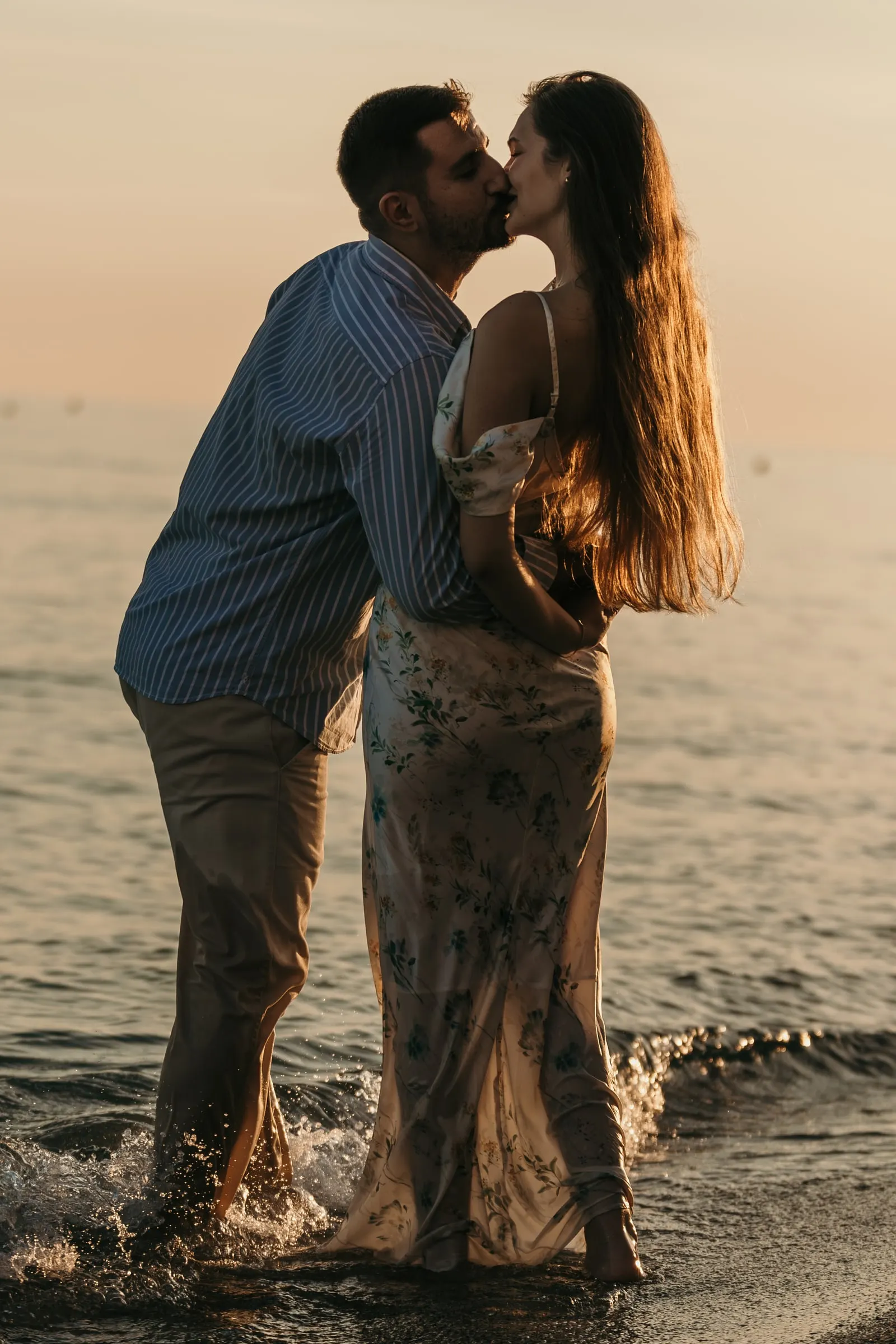 La pareja se besa mientras las olas salpican a sus pies al atardecer, en la playa de Nerja