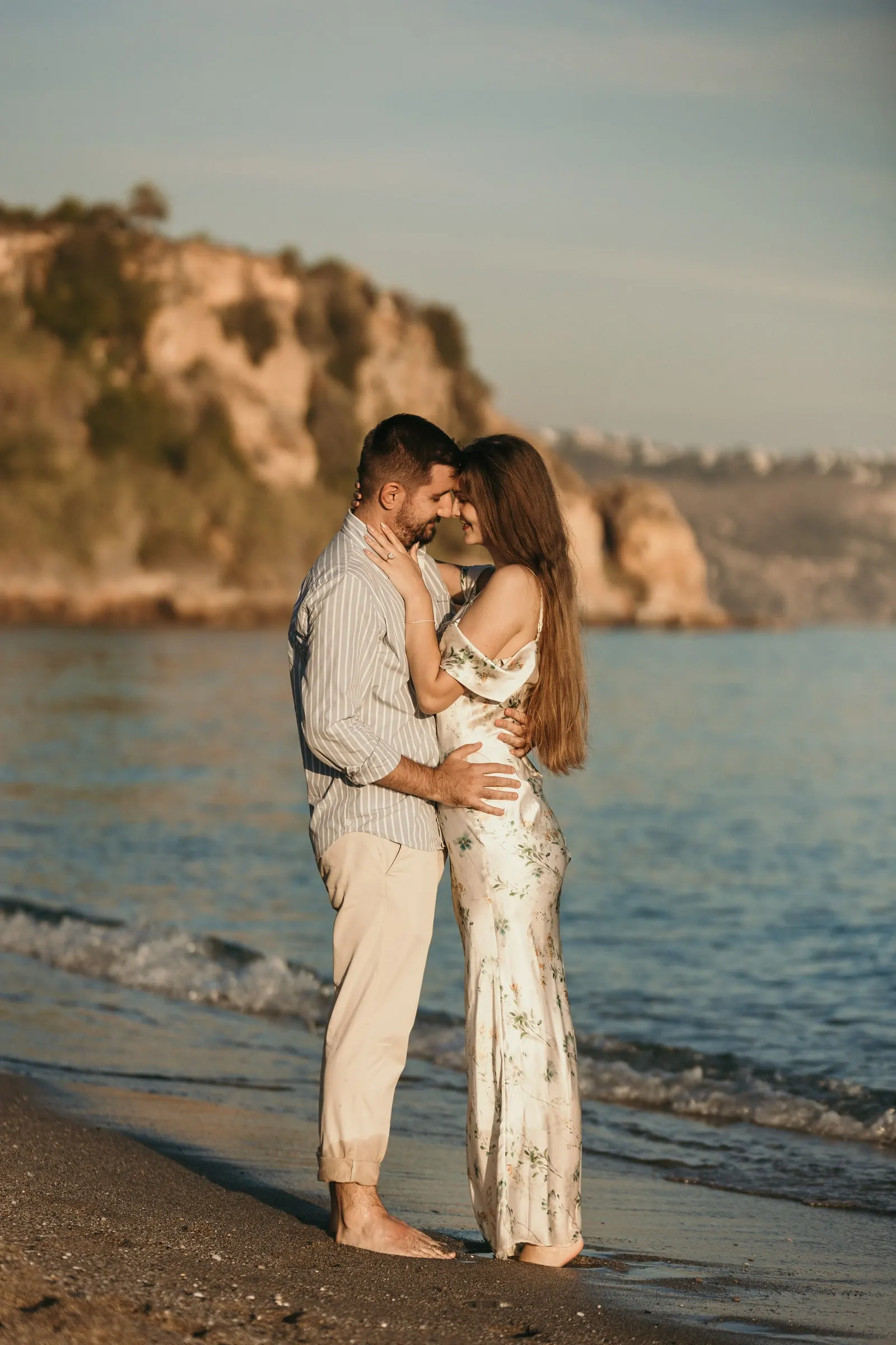 La pareja abrazada en la orilla con los acantilados al fondo, en la playa de Nerja