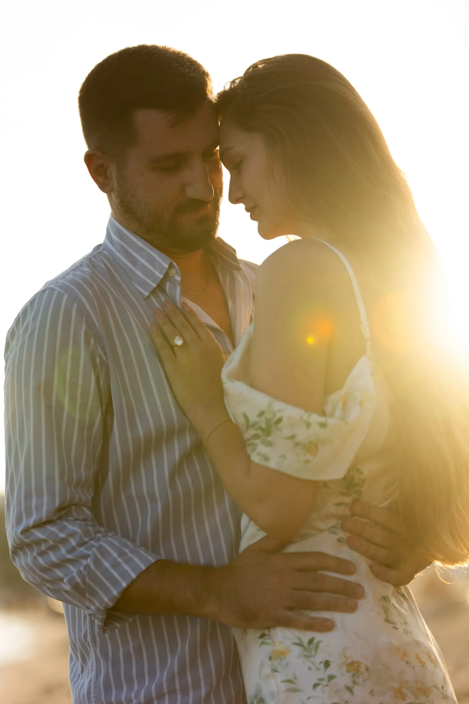 La pareja frente con frente con el sol detrás y el anillo a la vista, en la playa de Nerja