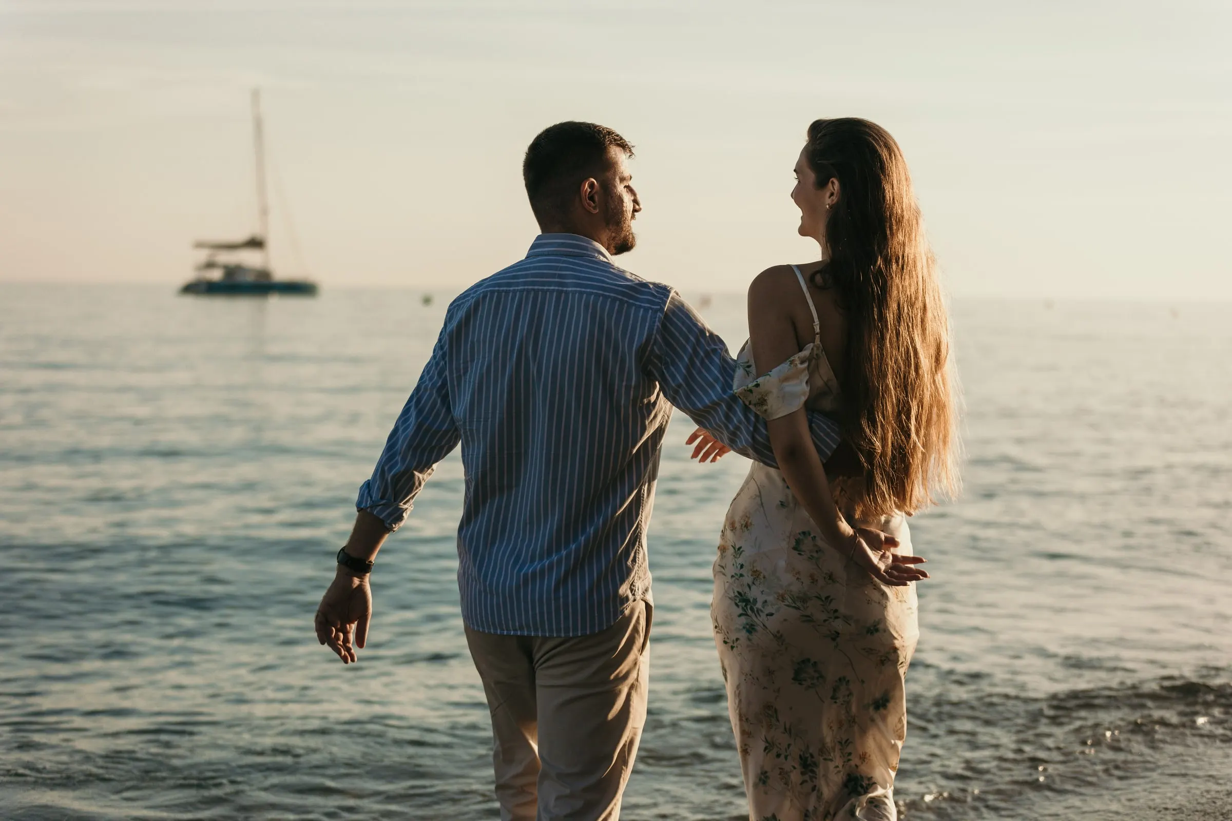 Couple walking into the sea hand in hand, a sailing boat on the horizon, beach in Nerja
