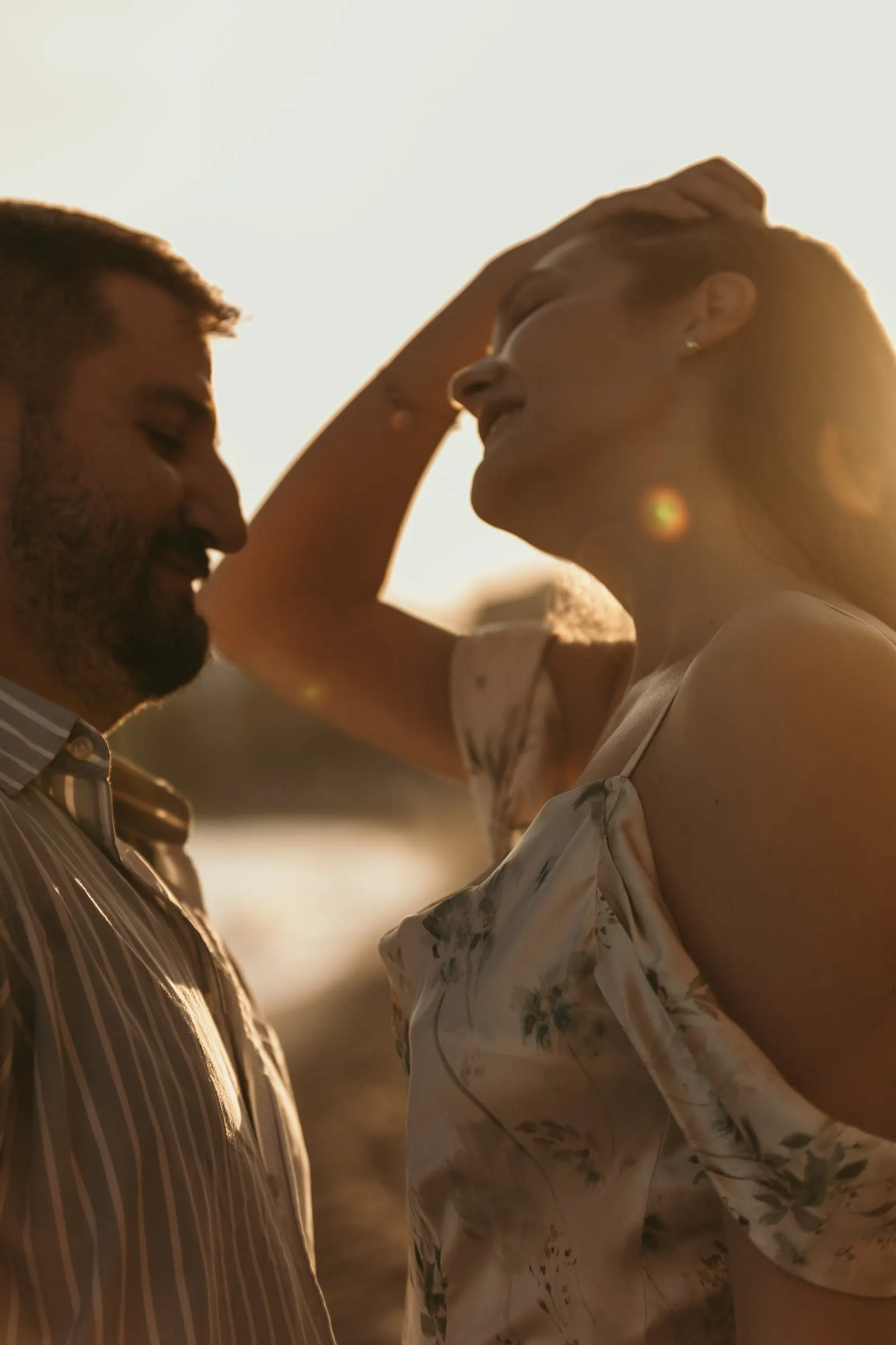 Ella se recoge el pelo y ríe mientras él le sonríe con la luz del atardecer, playa de Nerja