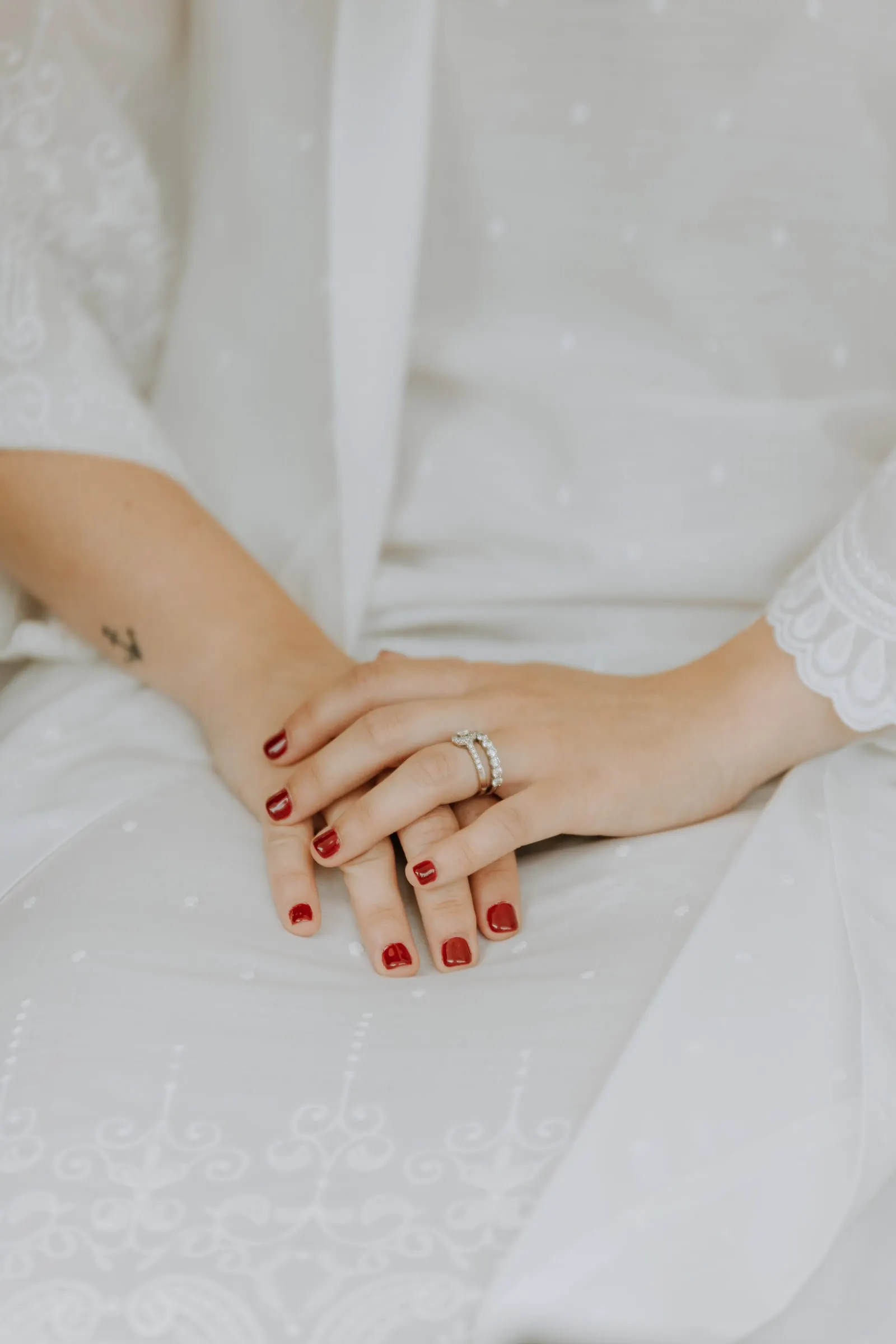Bride's hands with red nails and her engagement ring resting on white lace, wedding morning in Sotogrande