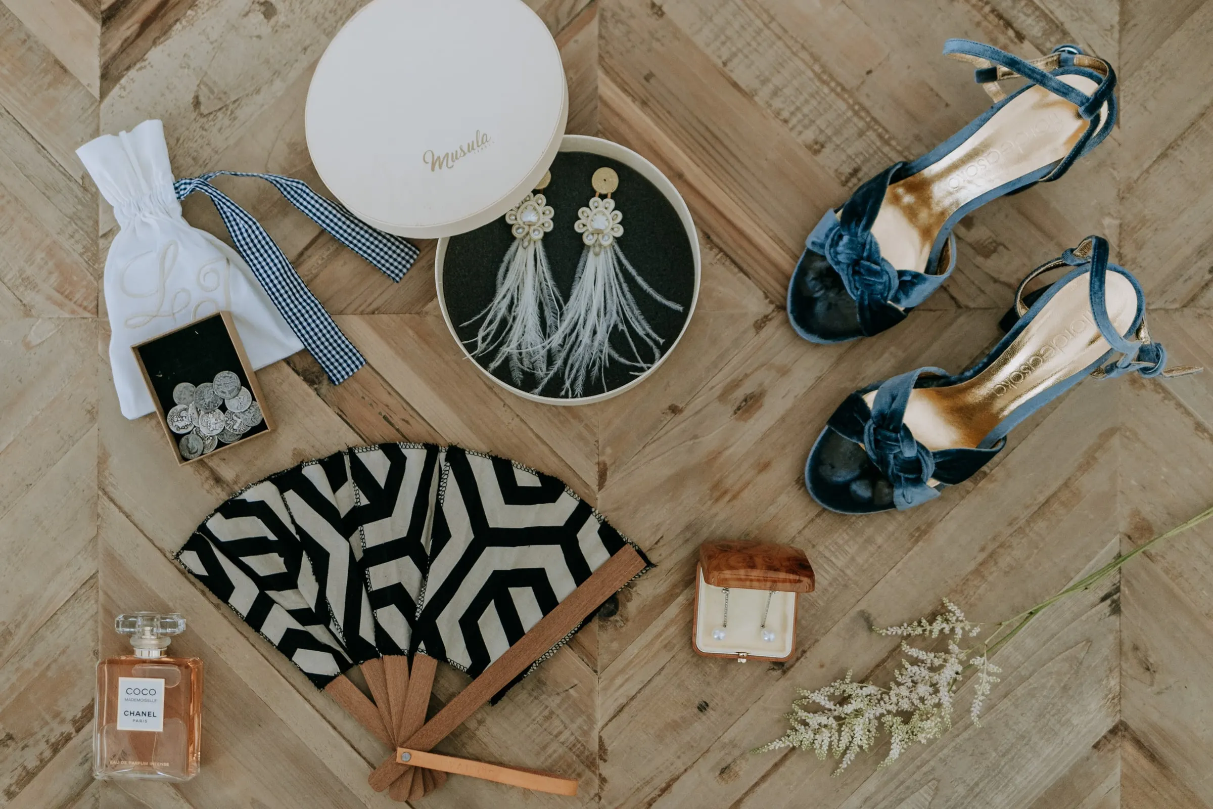 Blue velvet sandals, feather earrings, a fan and perfume laid out on wood before the wedding, Sotogrande