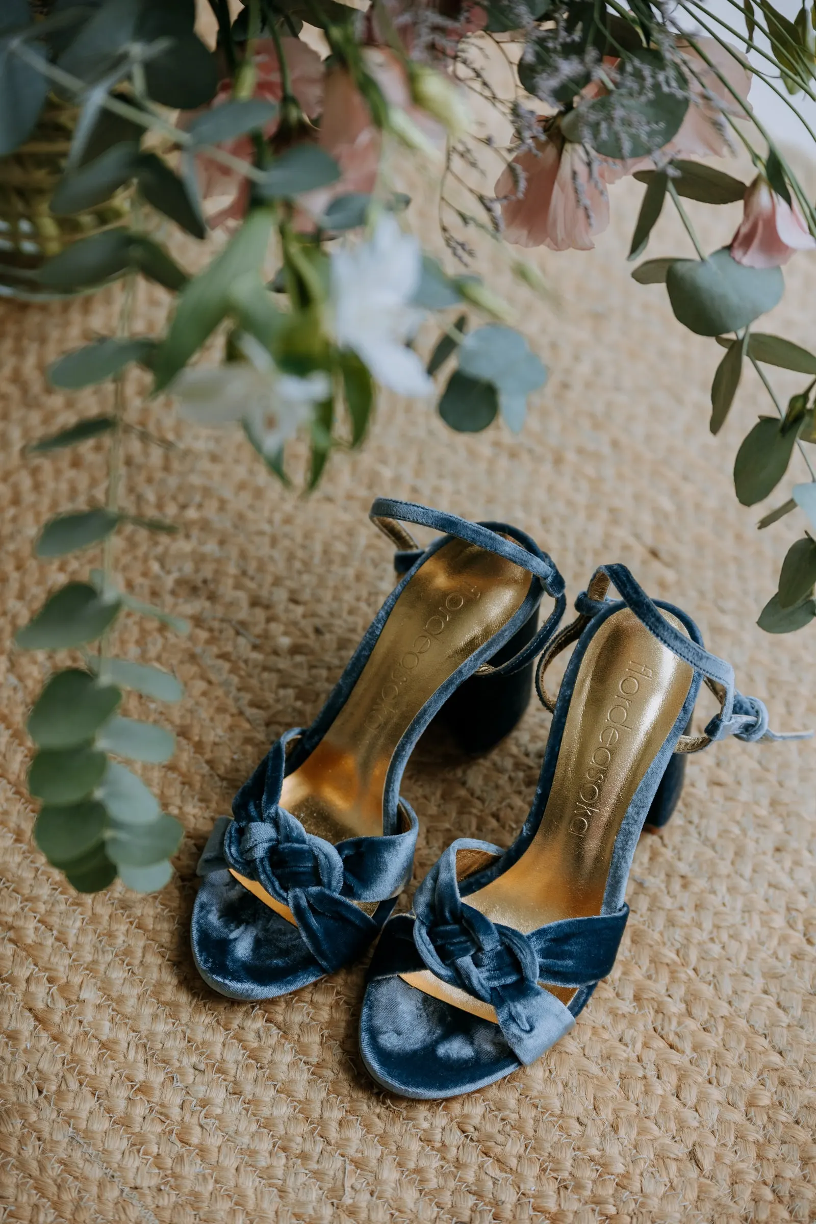 Blue velvet bridal sandals on a jute rug among eucalyptus