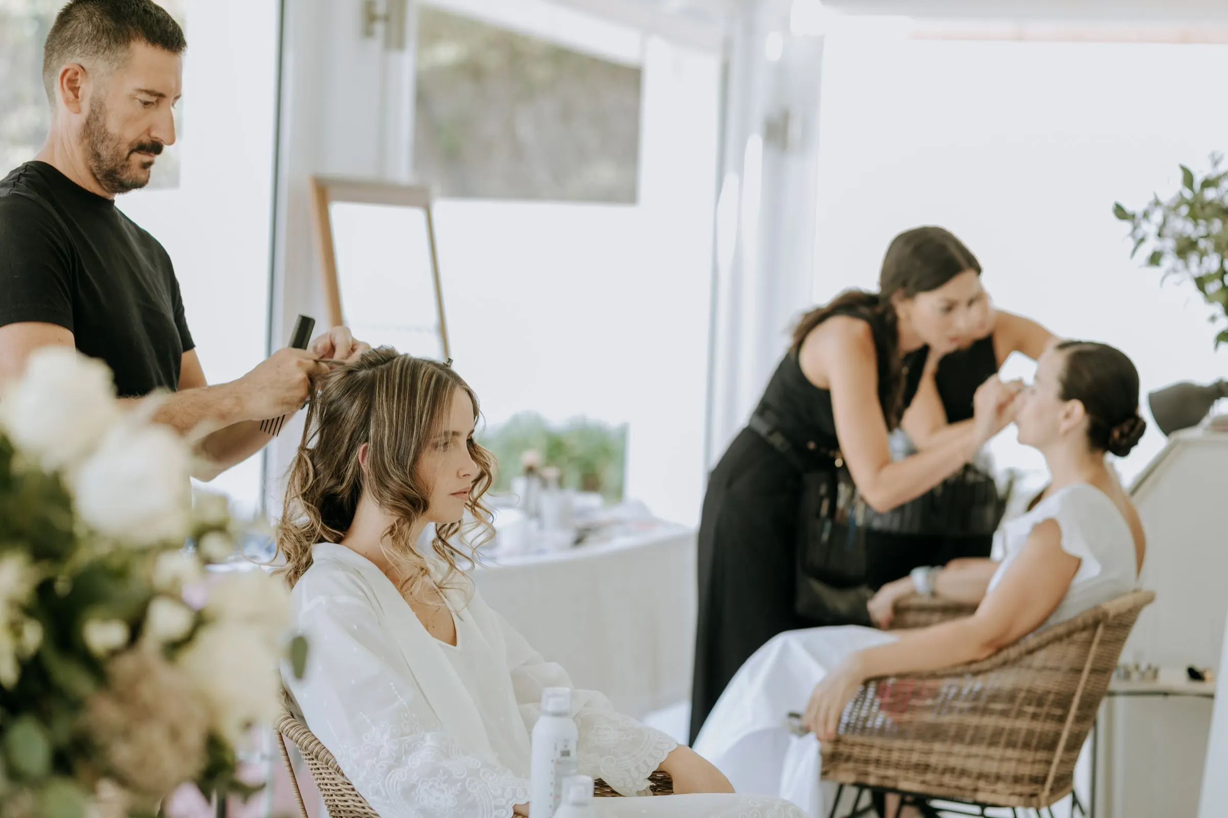 Hair and make-up artists at work in a bright white room on the wedding morning