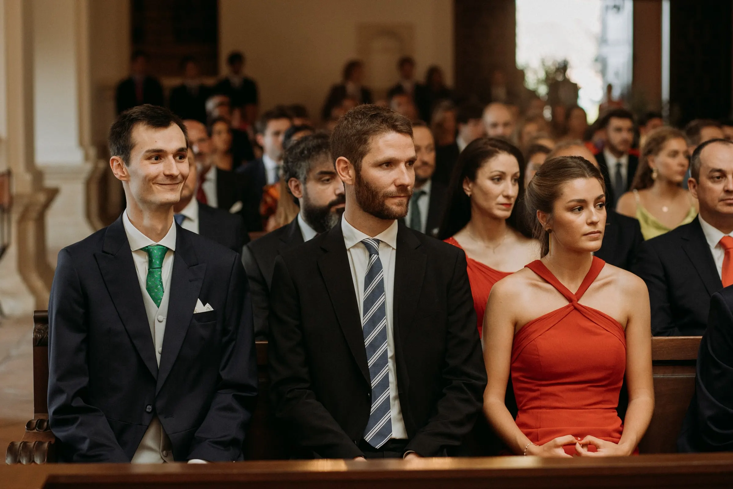 Guests in morning suits and a red halter dress standing in the packed pews of the church in Sotogrande