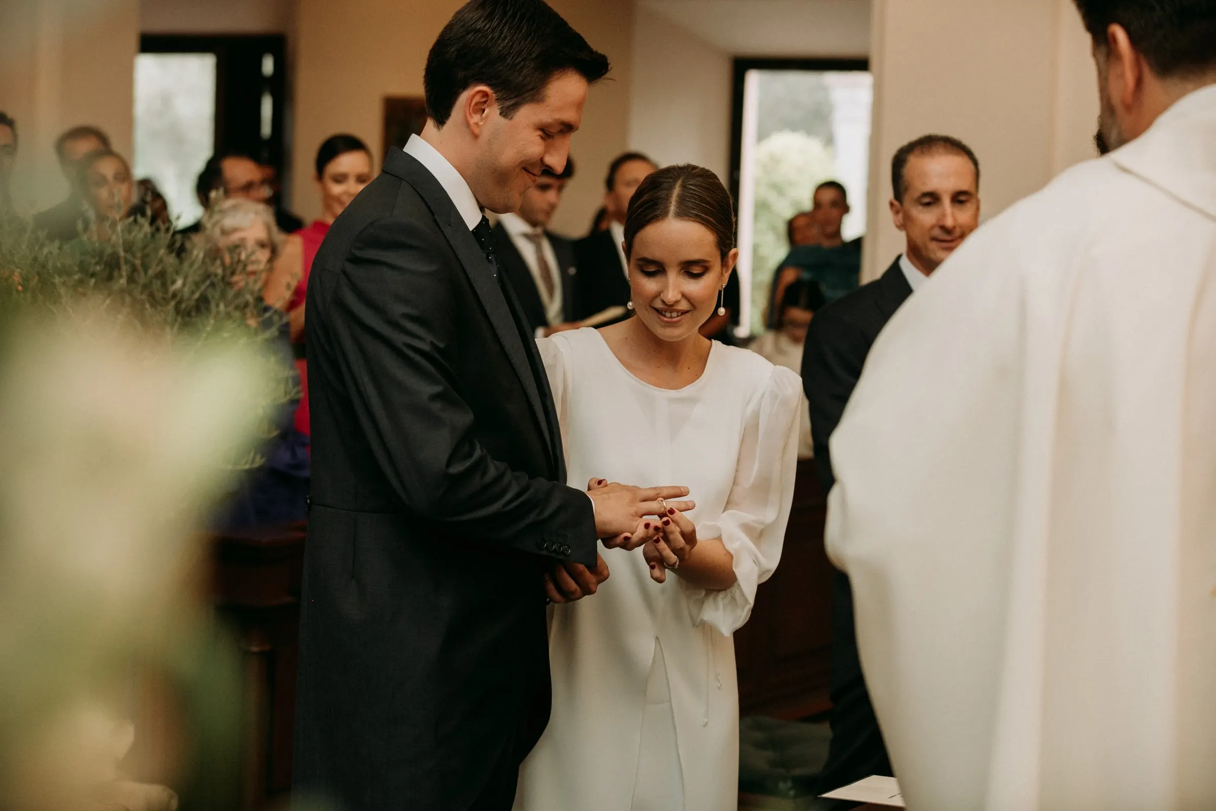 Bride slipping the wedding ring onto the groom's finger beside the priest in Sotogrande