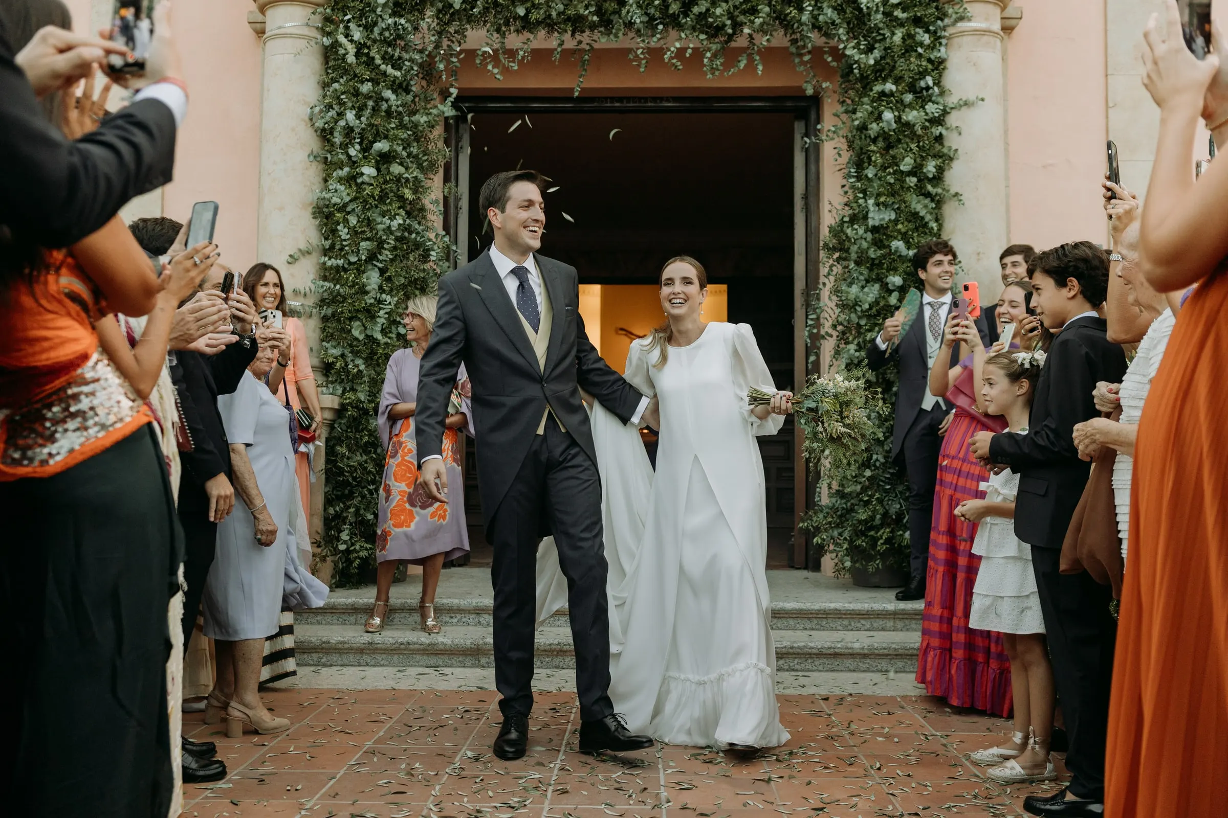 Newlyweds leaving the ivy-framed church as guests hold up their phones, Nuestra Señora de la Merced, Sotogrande