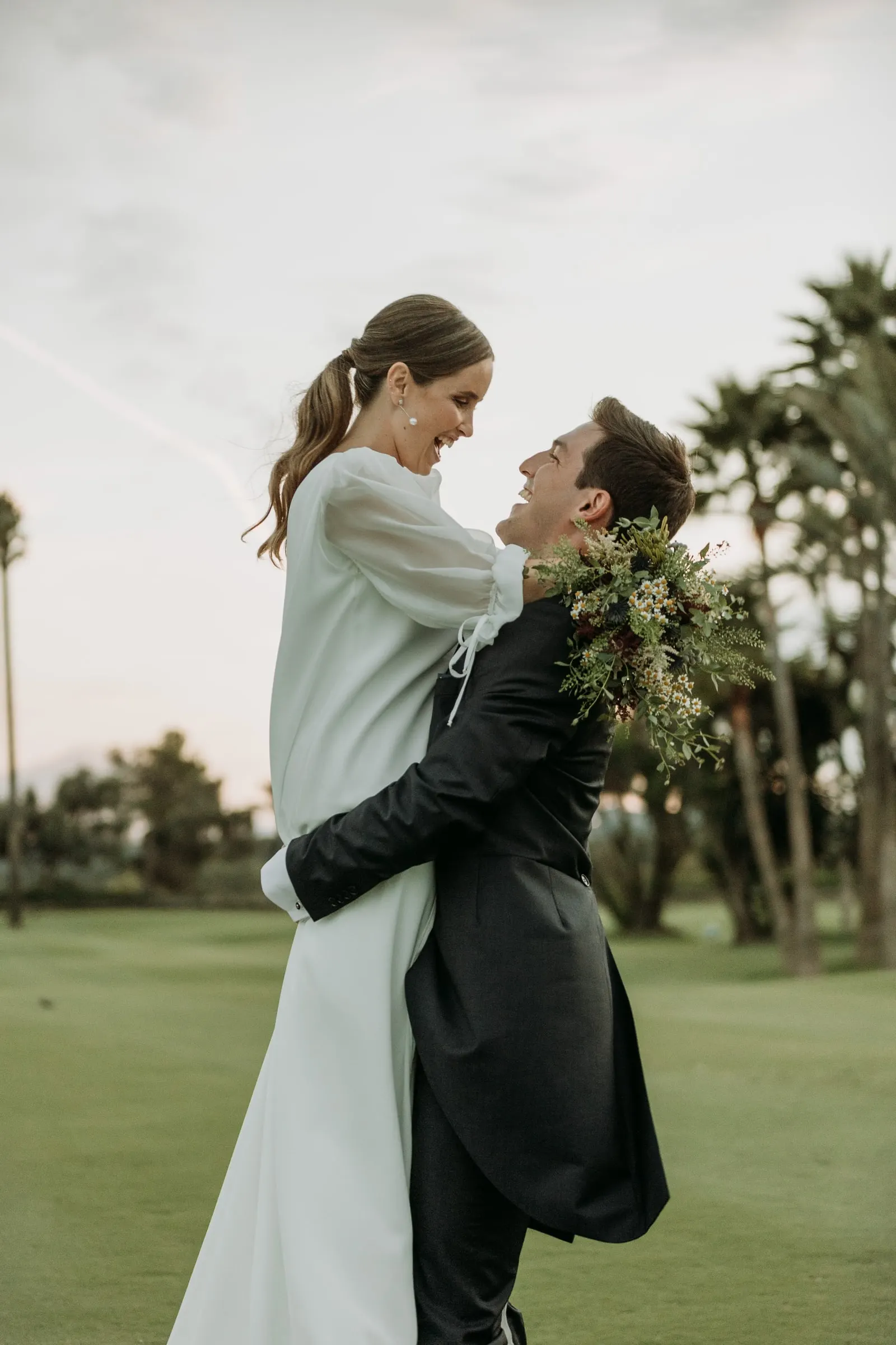 Groom lifting the bride on the golf course at sunset, palm trees behind, Sotogrande