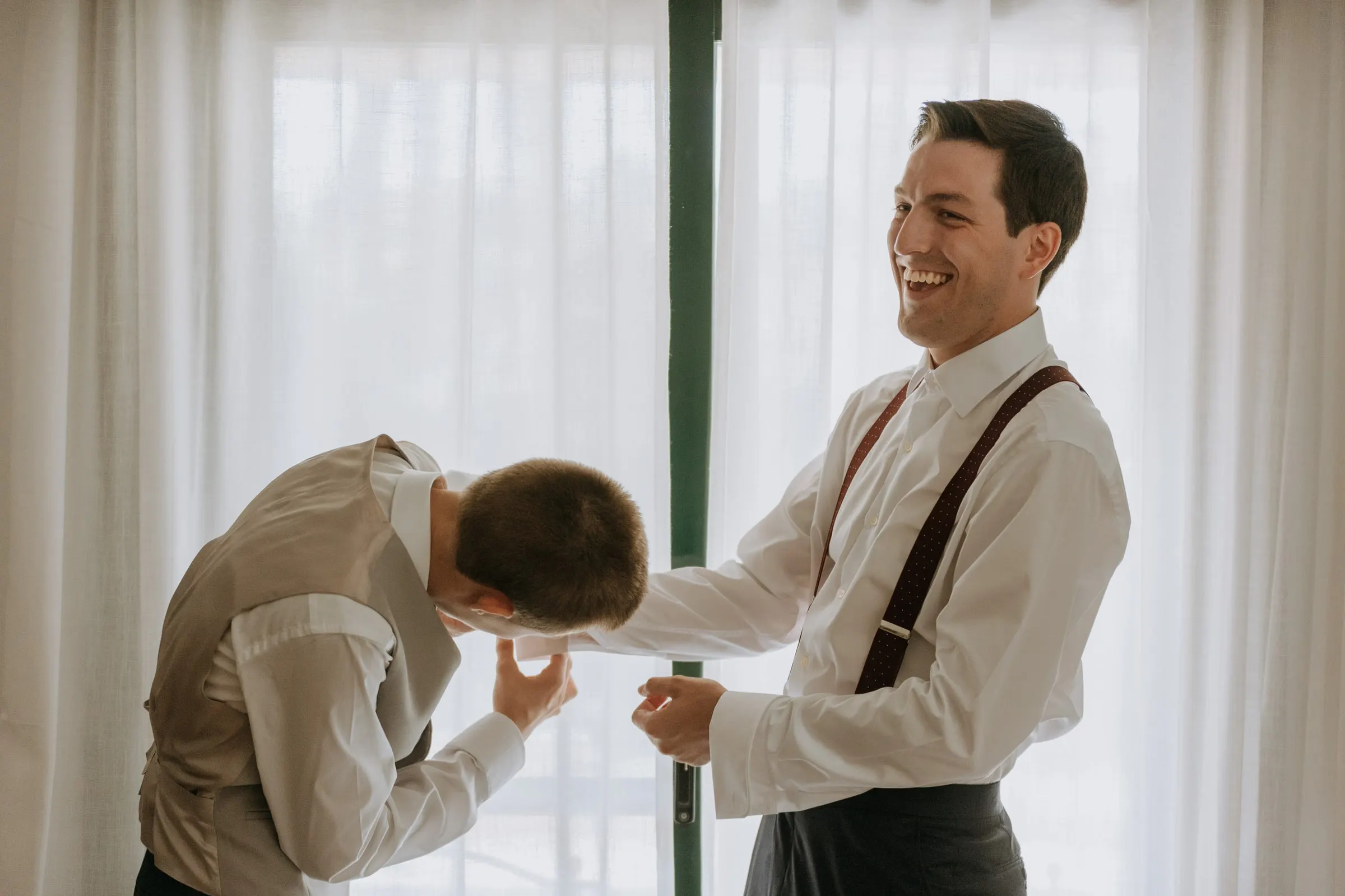 Groom laughing with a friend while getting dressed for the wedding