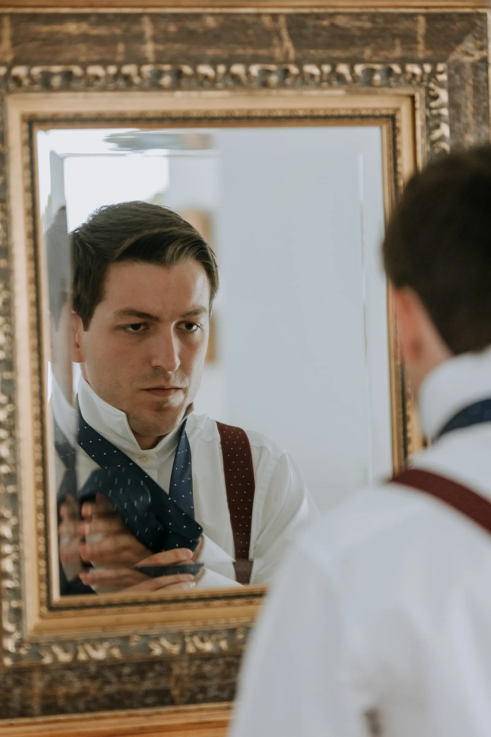 Groom reflected in a gilded mirror as he finishes dressing in Sotogrande