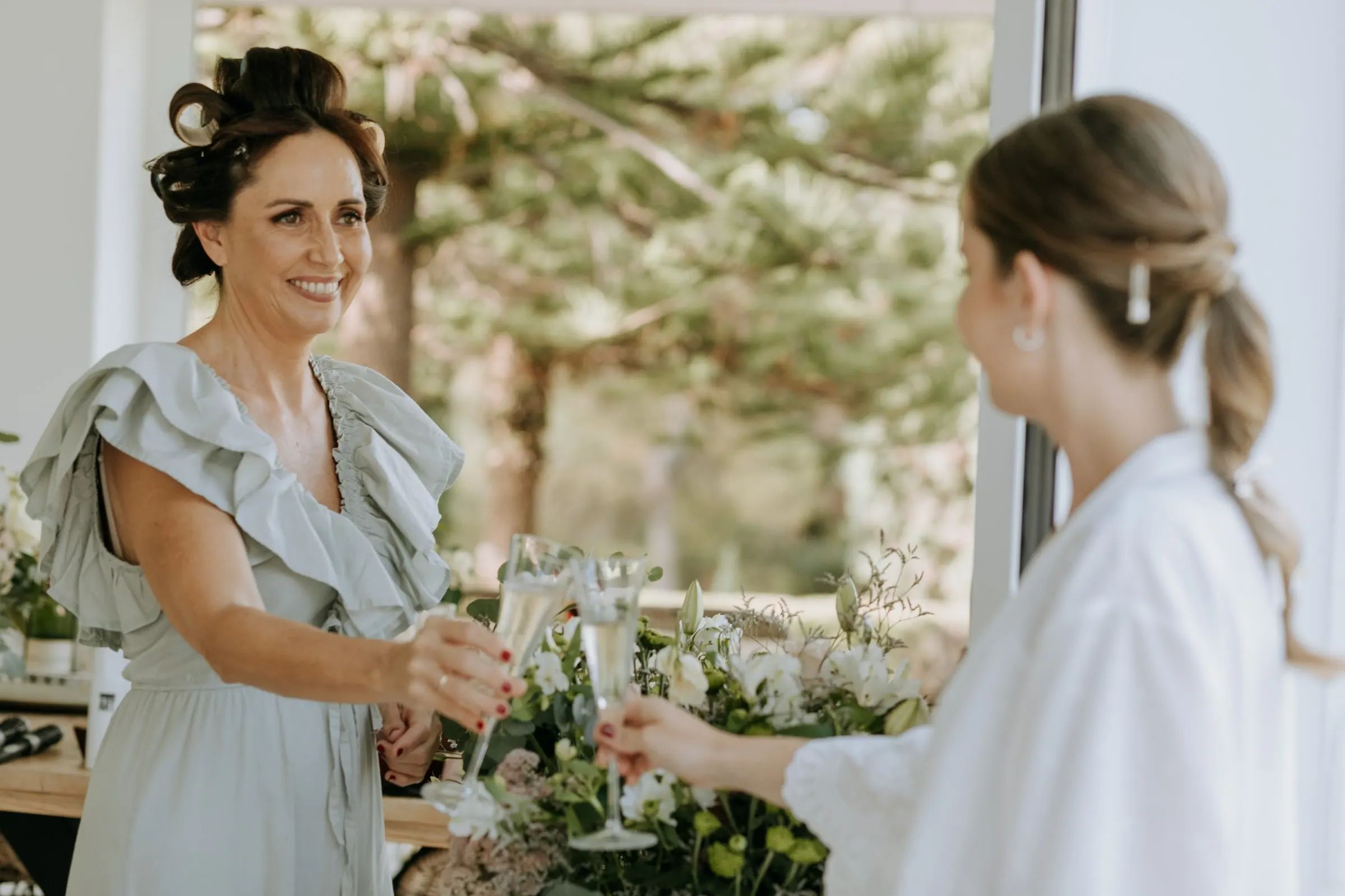 Bride toasting with a guest in sage green, champagne glasses in hand