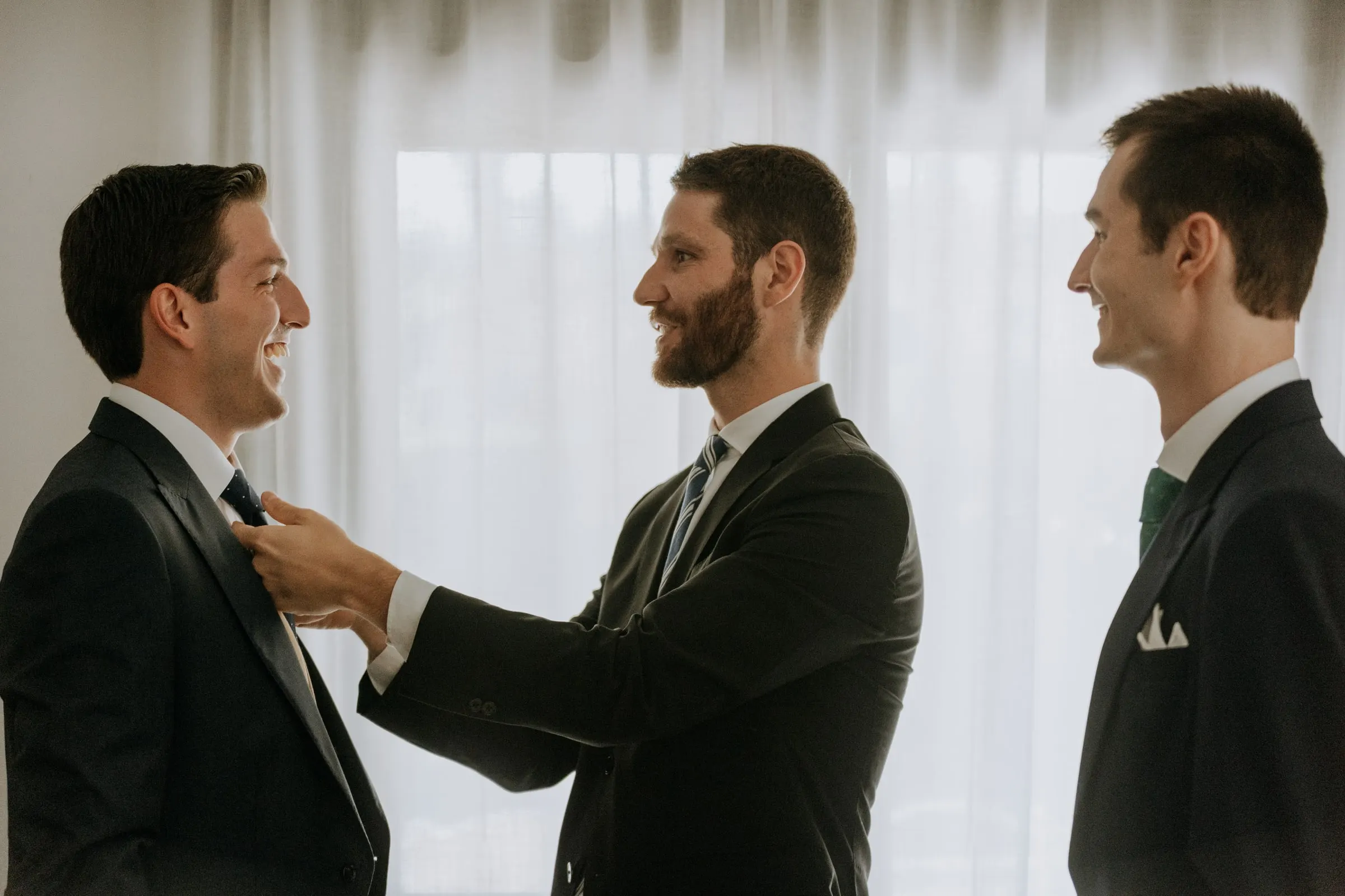 Friend straightening the groom's tie while the groomsmen look on