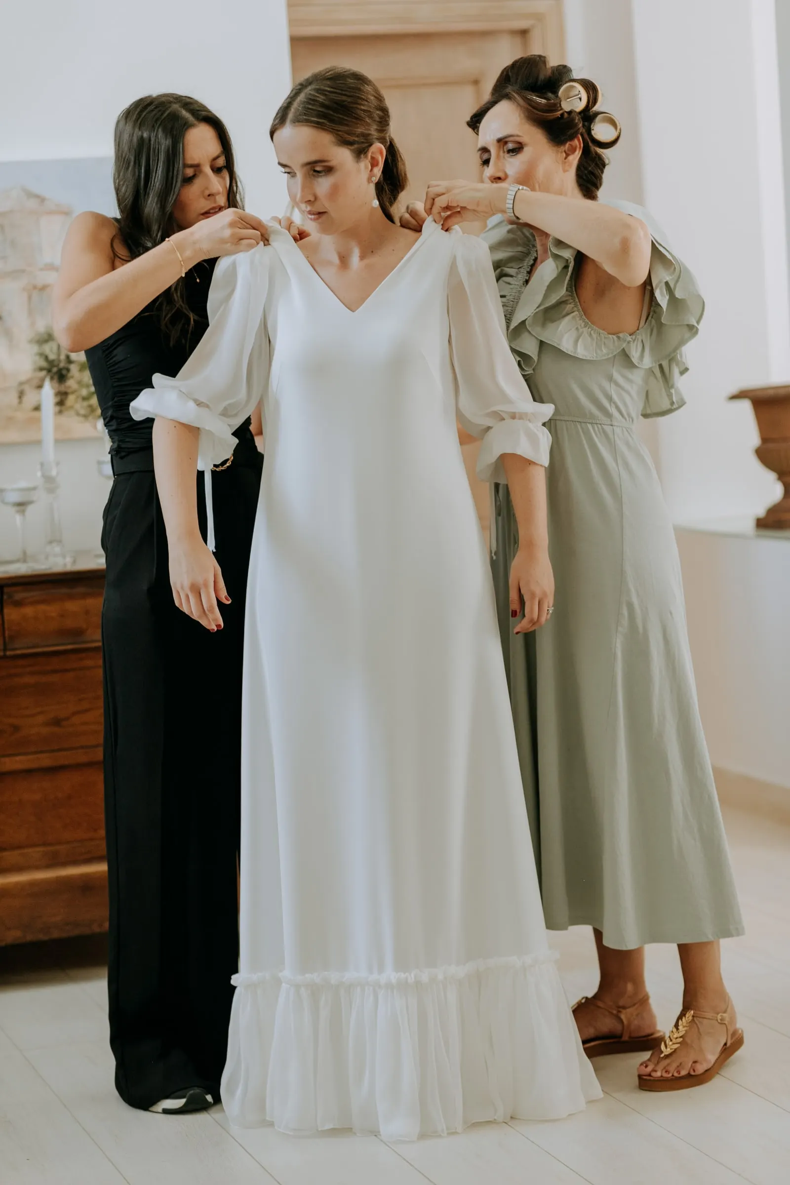 Two women helping the bride into her long-sleeved dress