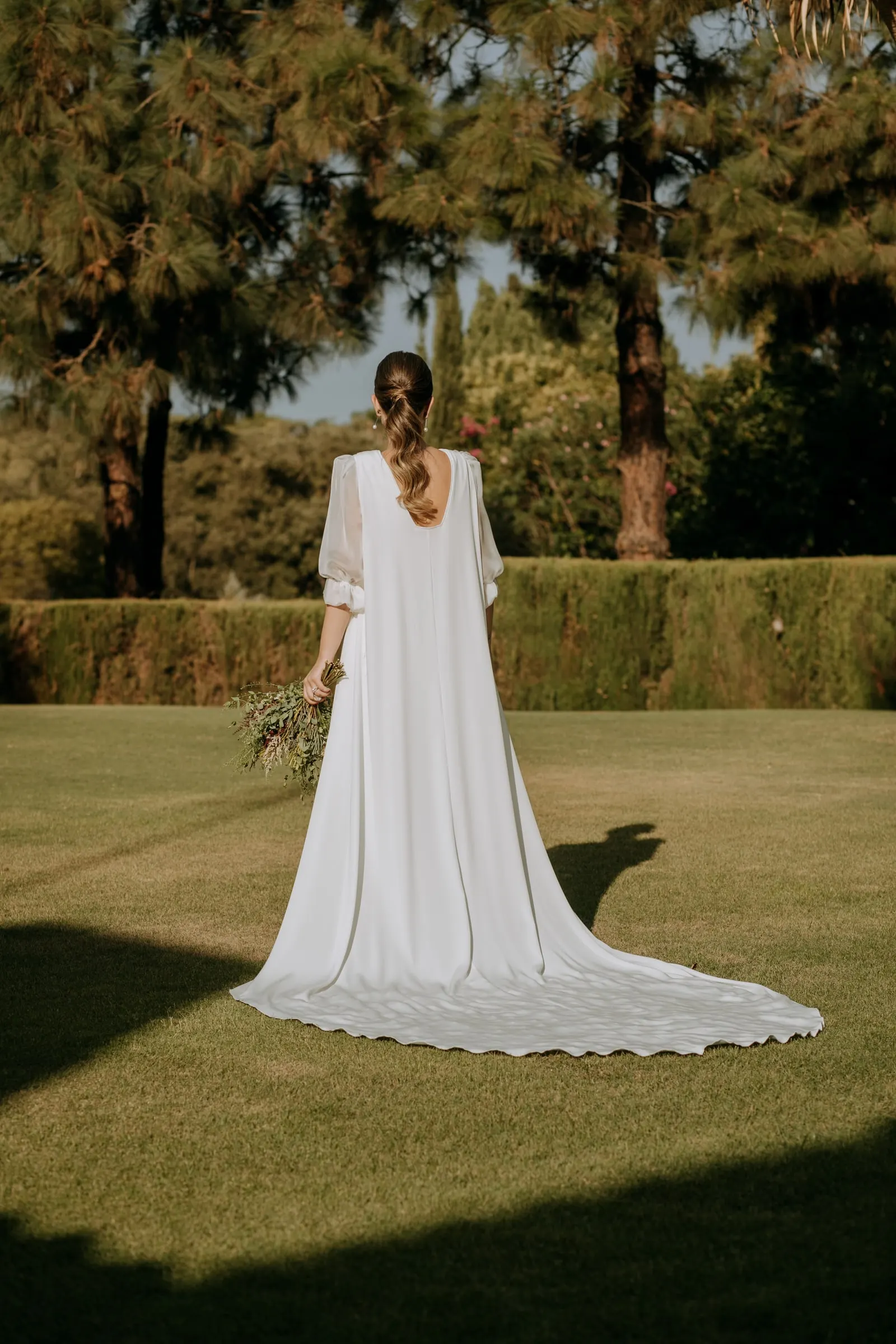 Bride from behind on the lawn, the open back and train of her dress