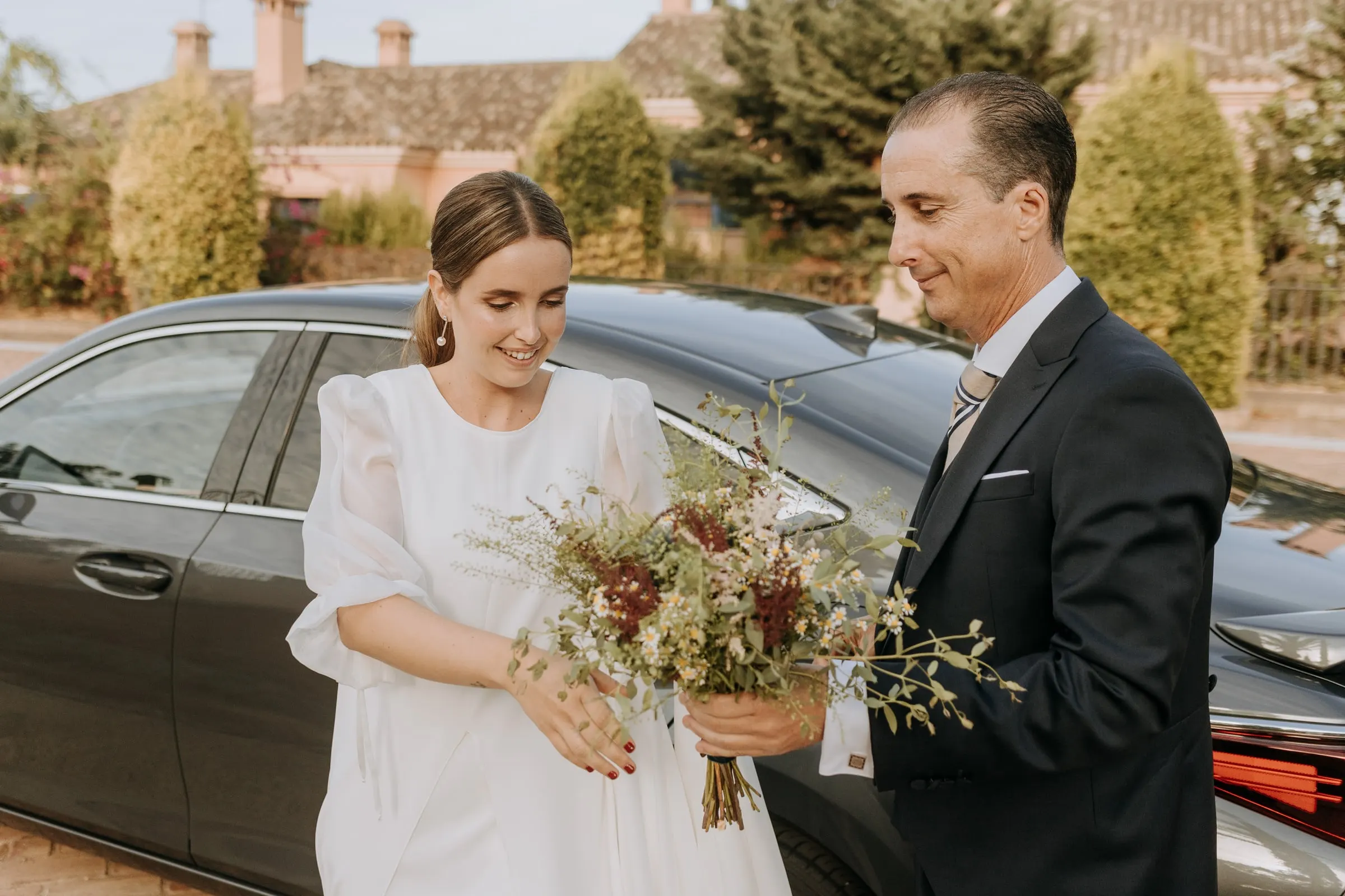 Bride's father handing her the bouquet as she steps out of the car at the church in Sotogrande