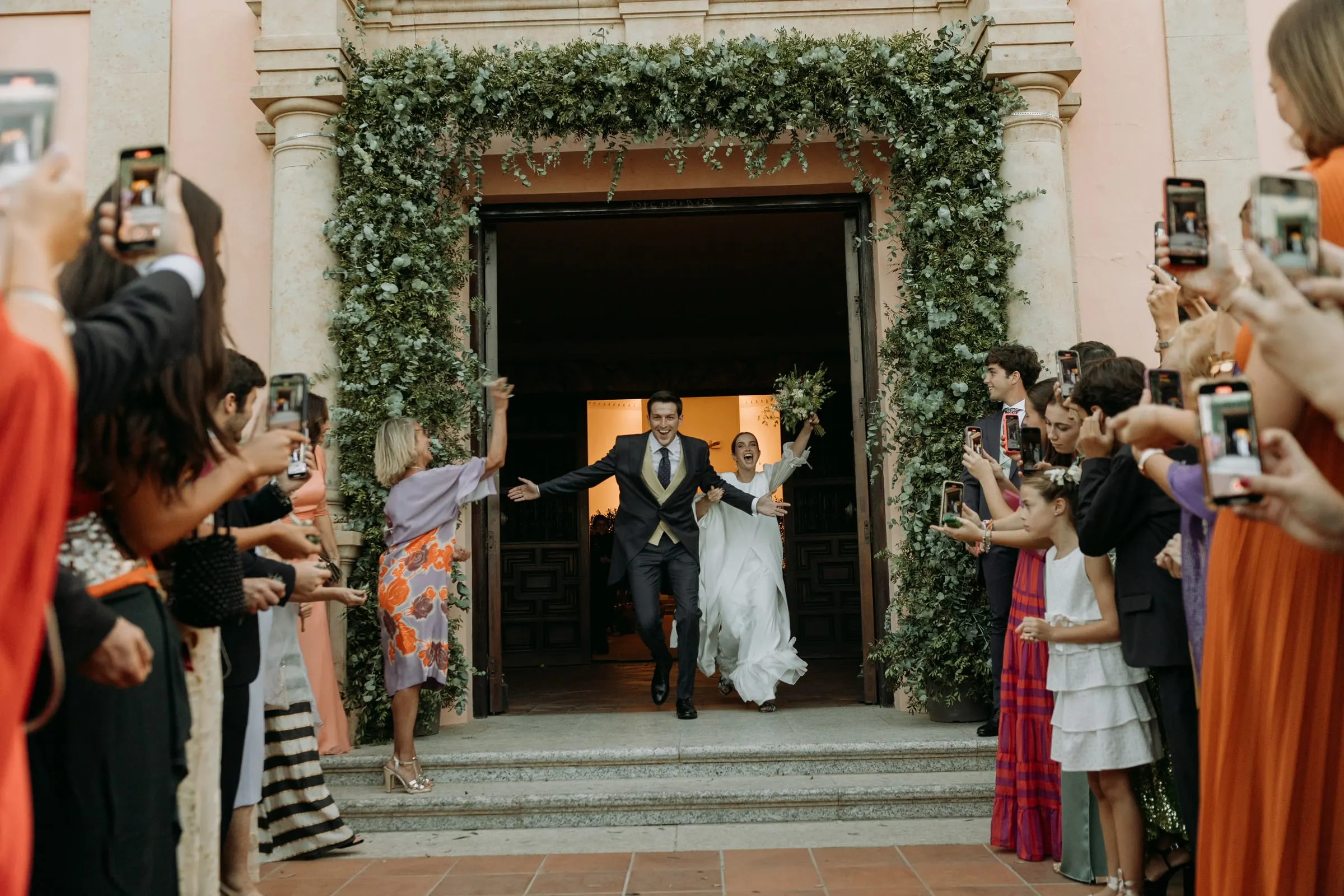 Los recién casados salen de la iglesia por la puerta enmarcada de verde mientras los invitados graban, Sotogrande