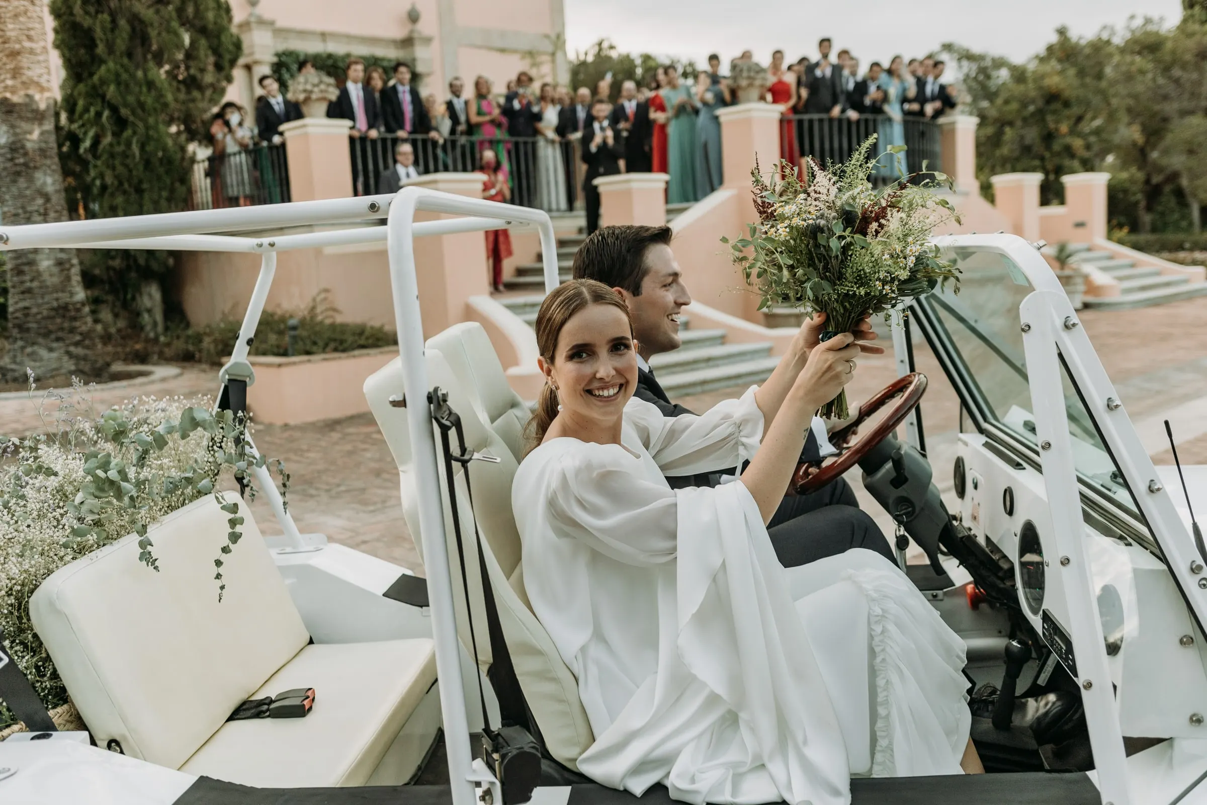 Bride laughing in a white open-top car decorated with gypsophila