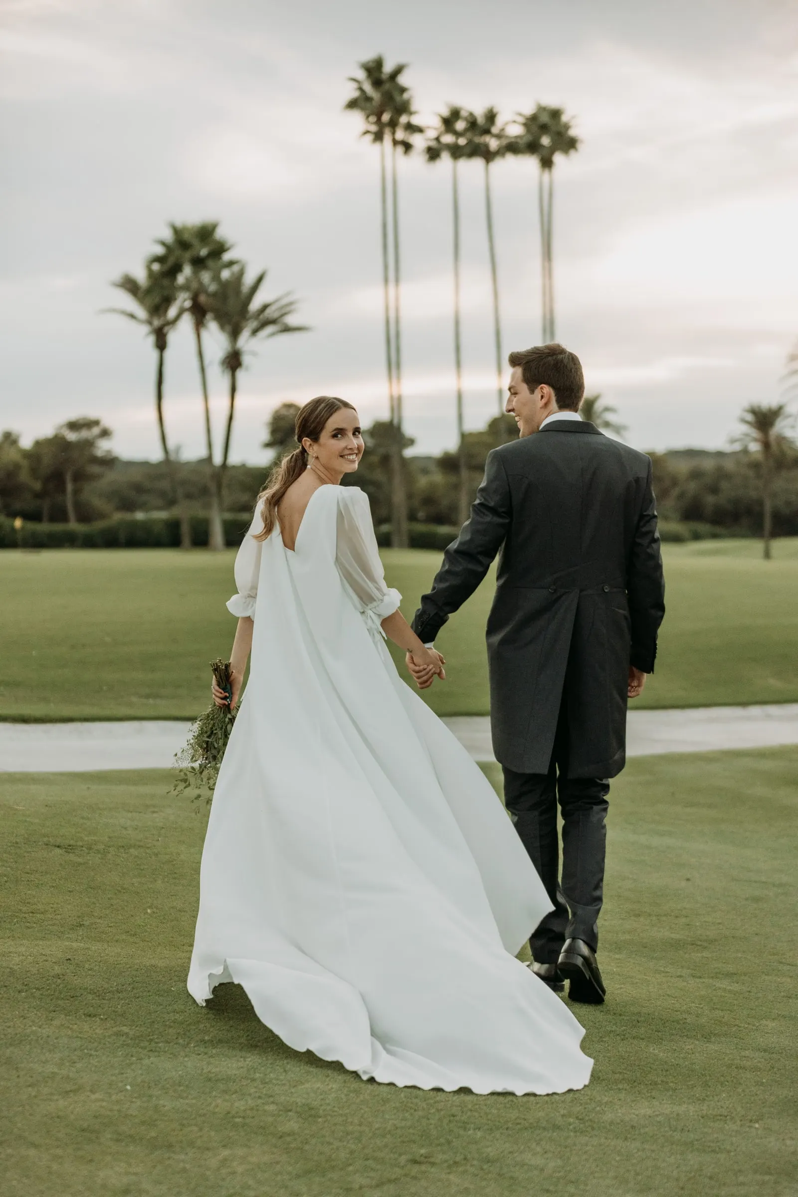 Bride and groom walking hand in hand across the fairway