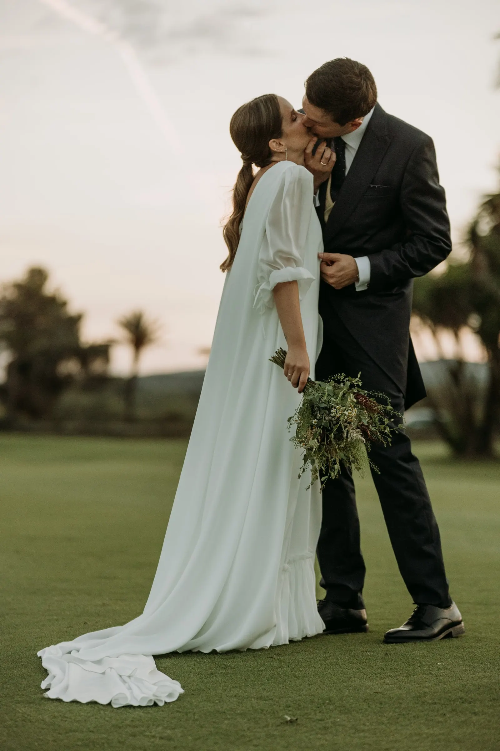 El novio besa a la novia en el campo de golf, con la cola sobre la hierba
