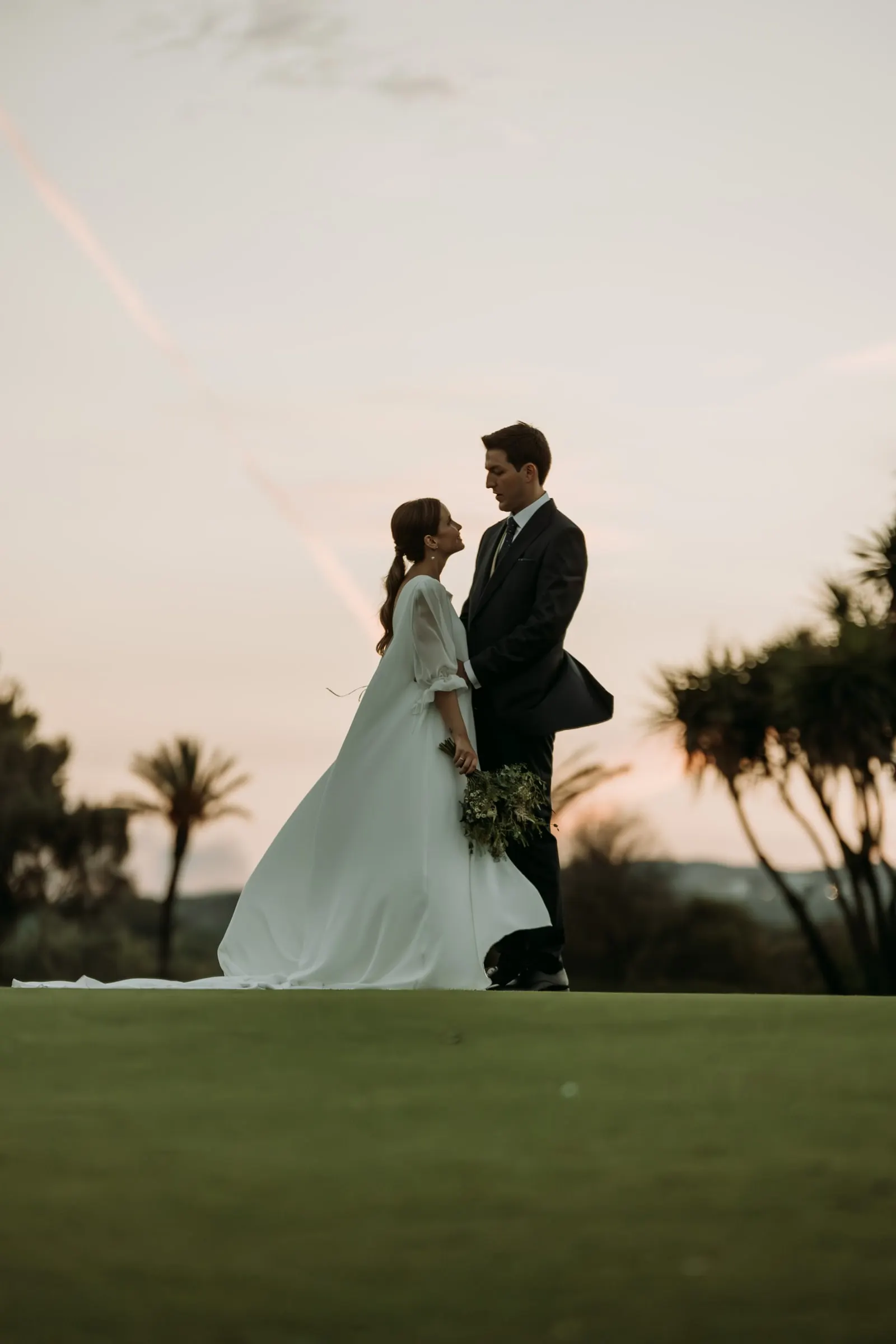 Los novios a contraluz contra el cielo del atardecer entre palmeras