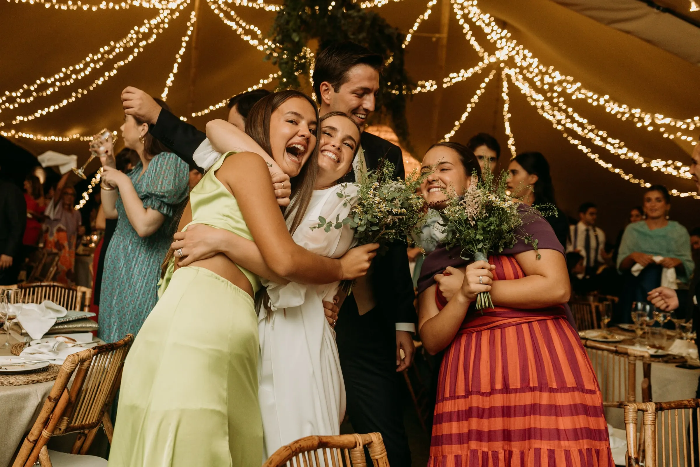Bride and her friends cheering with the bouquet among the tables
