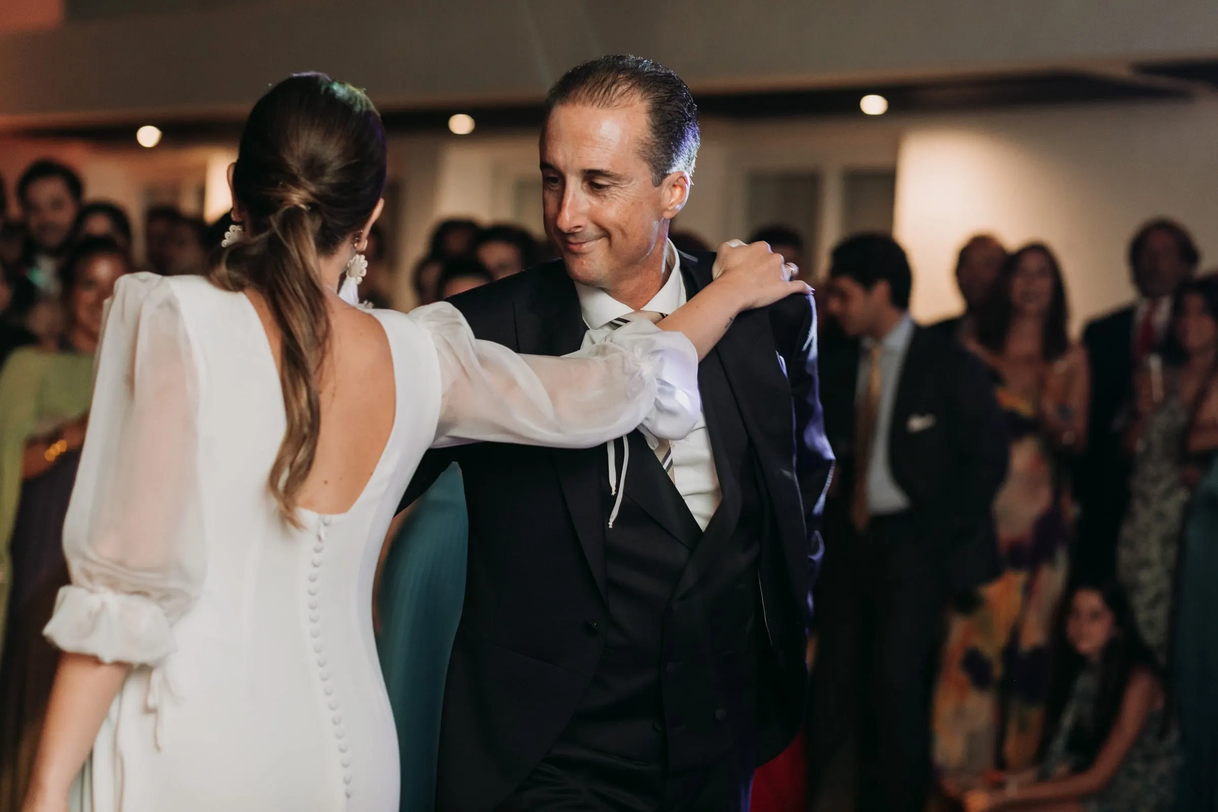 Bride dancing with a guest, seen from behind with her open back