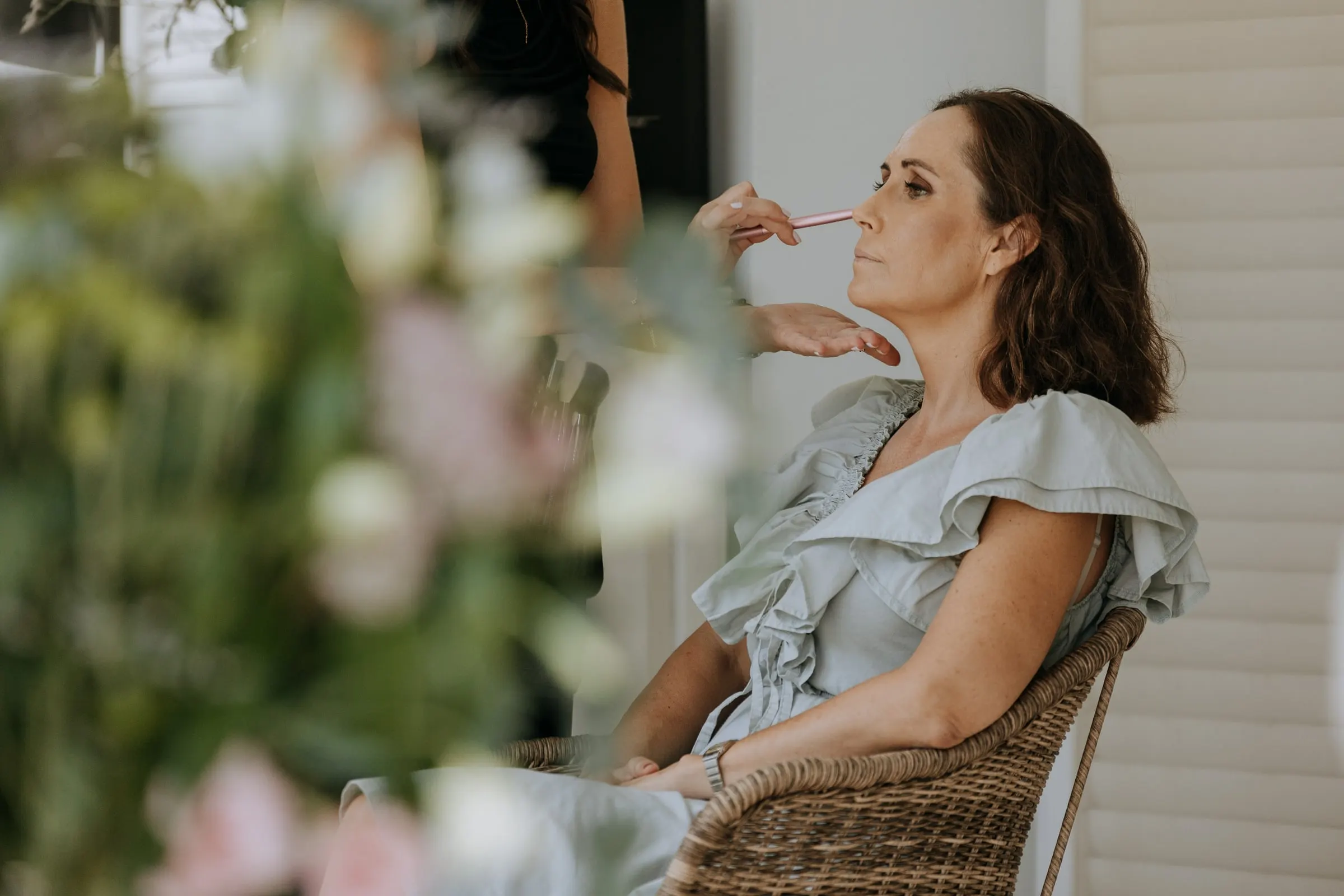 Guest in a pale blue ruffled dress having her make-up done in a wicker chair, Sotogrande