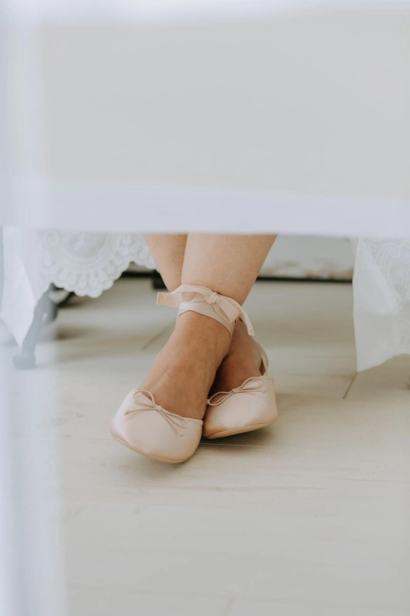 Pale pink ballet flats with ankle ribbons under a lace-edged table on the wedding morning