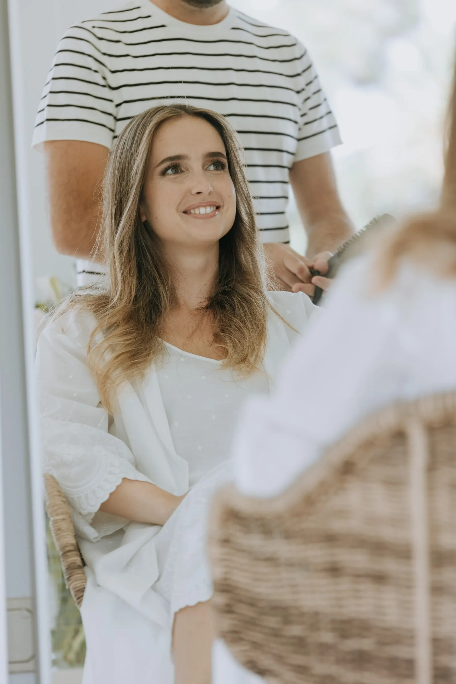 Bride smiling while a hairdresser in a striped T-shirt styles her hair on the wedding morning in Sotogrande