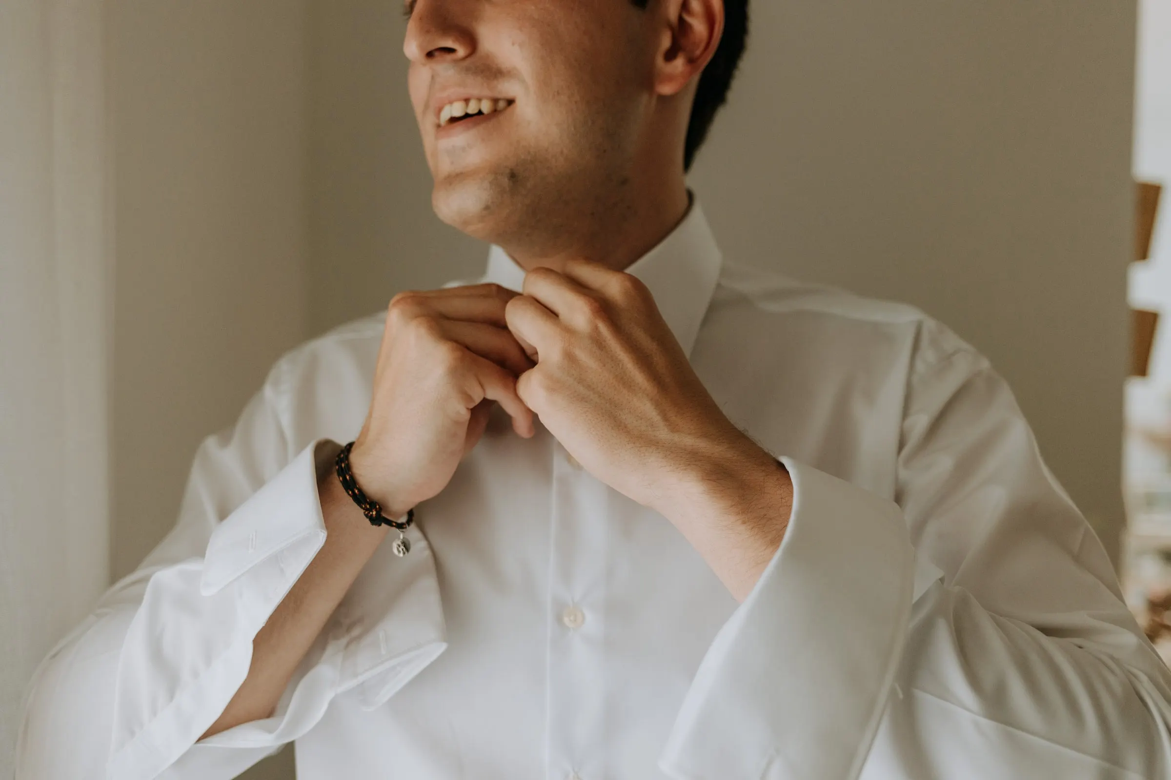 Groom laughing as he fastens the collar of his white shirt