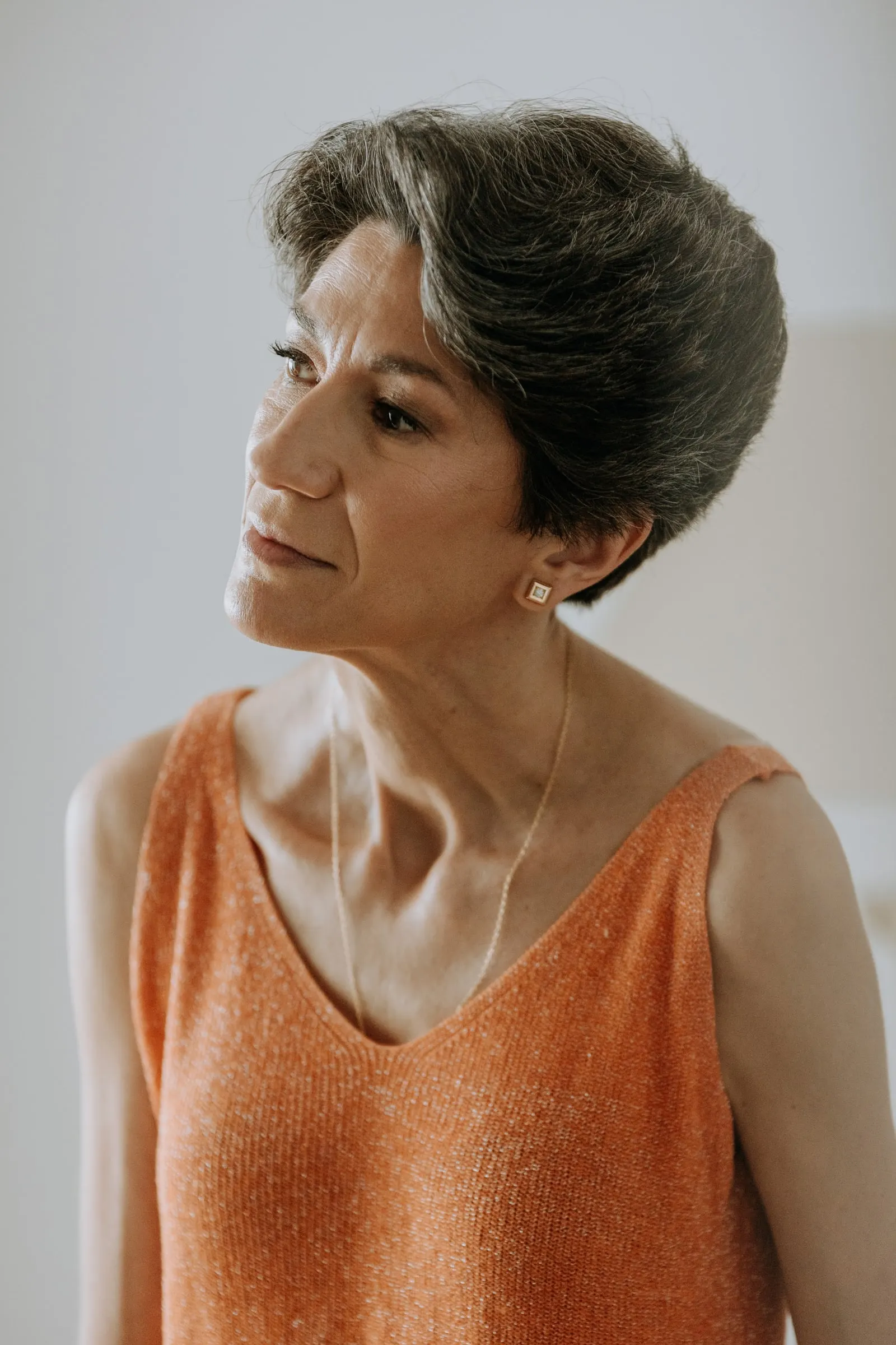 Woman with short dark hair in an orange top, in profile in the soft window light