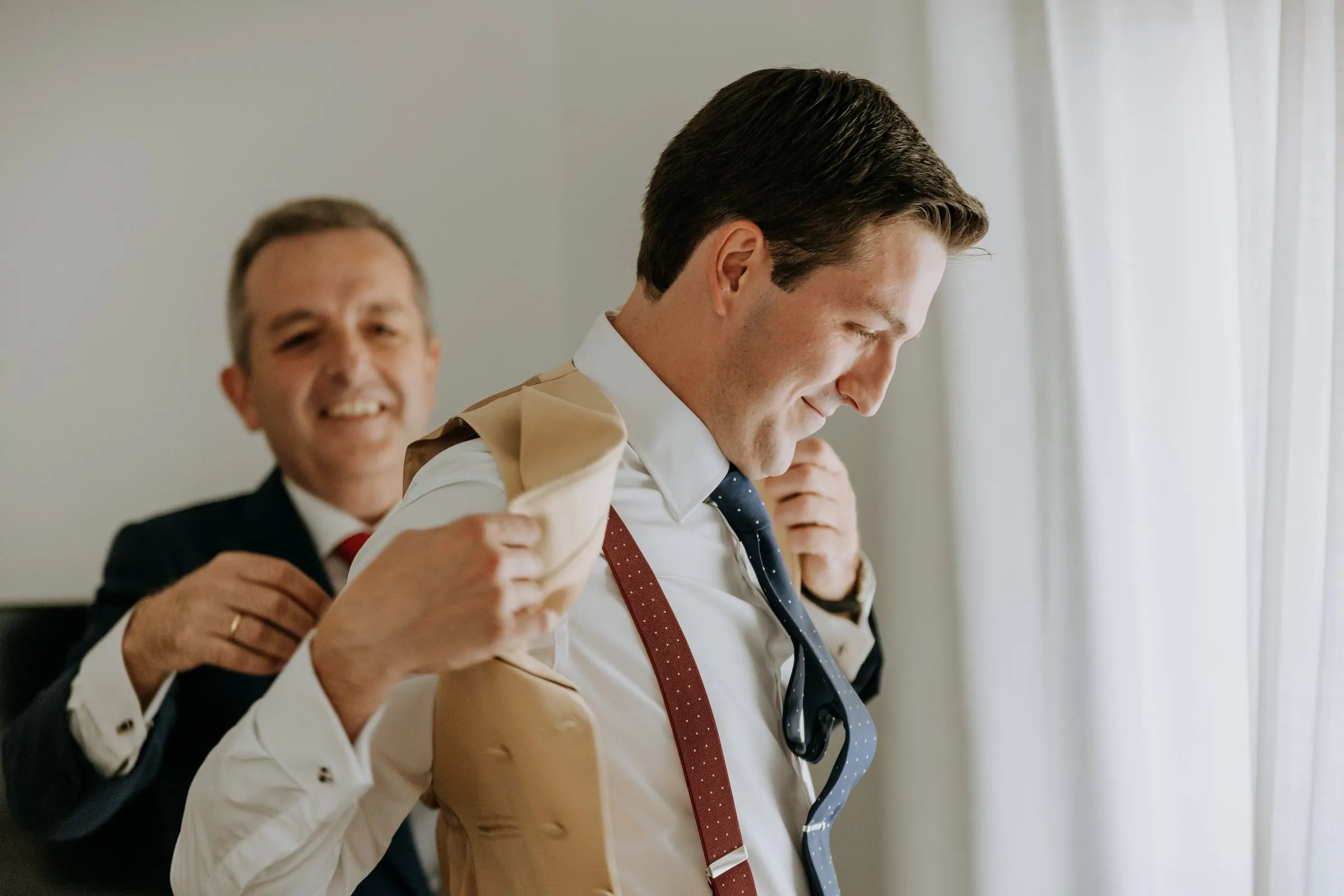 Groom and an older guest in a navy suit laughing over a gift wrapped in brown paper