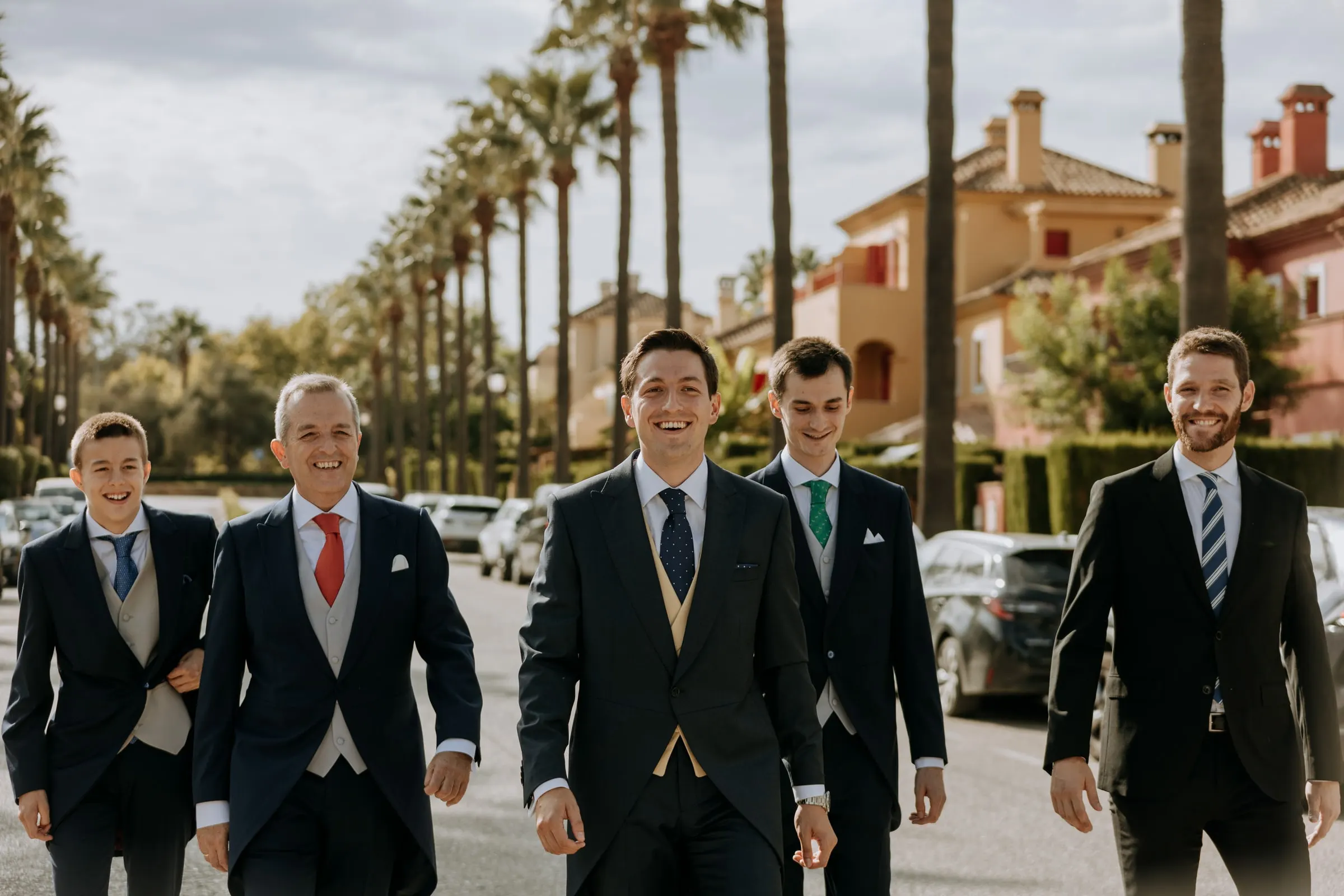 Groom and his men striding closer along the palm-lined avenue, terracotta houses of Sotogrande behind