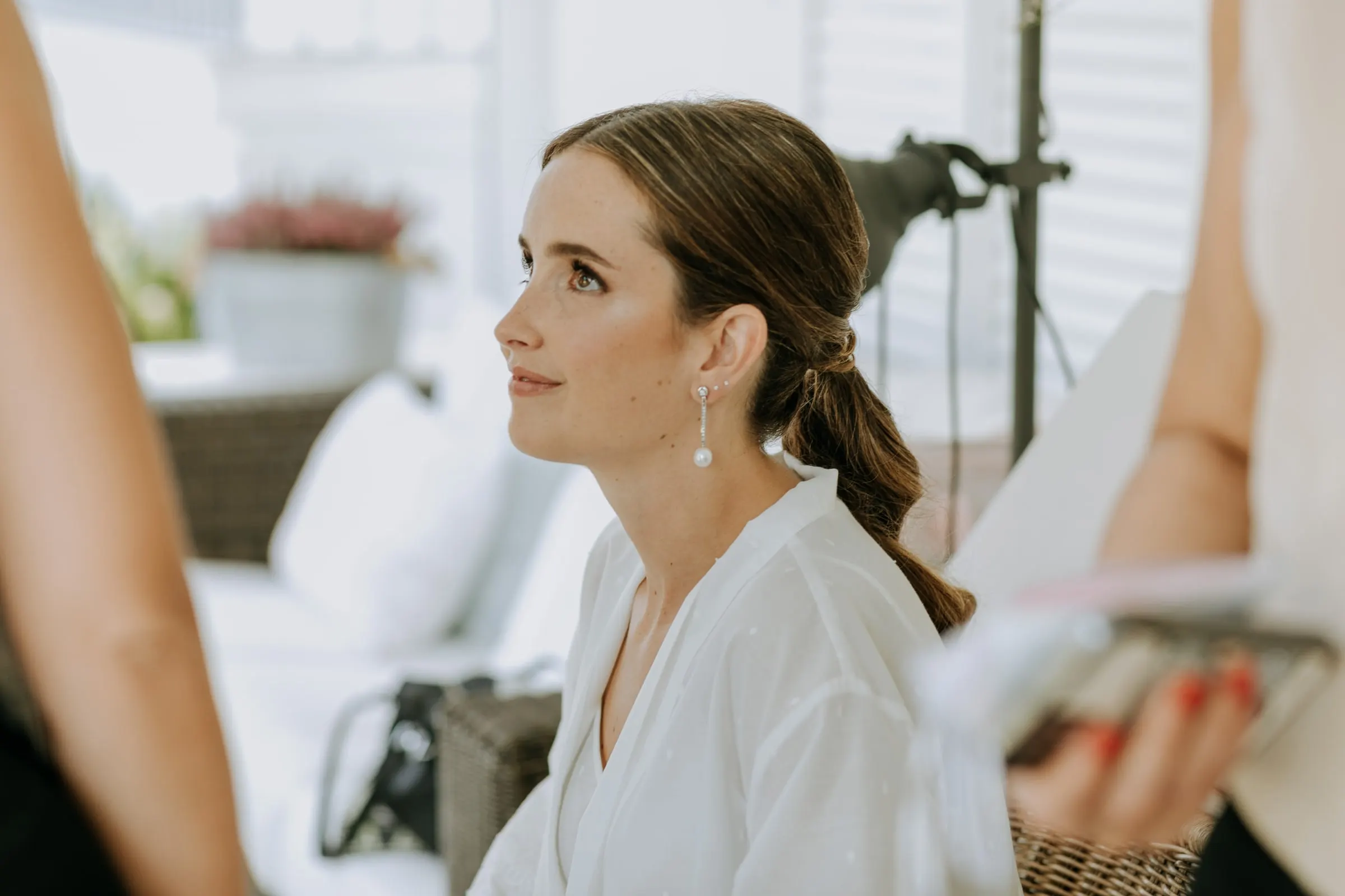 Bride in profile with her hair in a low ponytail and pearl earrings, getting ready in the white room