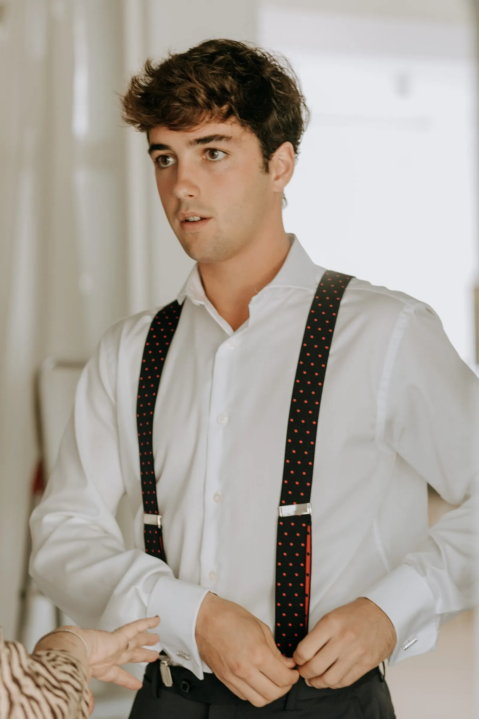 Groom's younger brother in black braces buttoning his shirt before the wedding