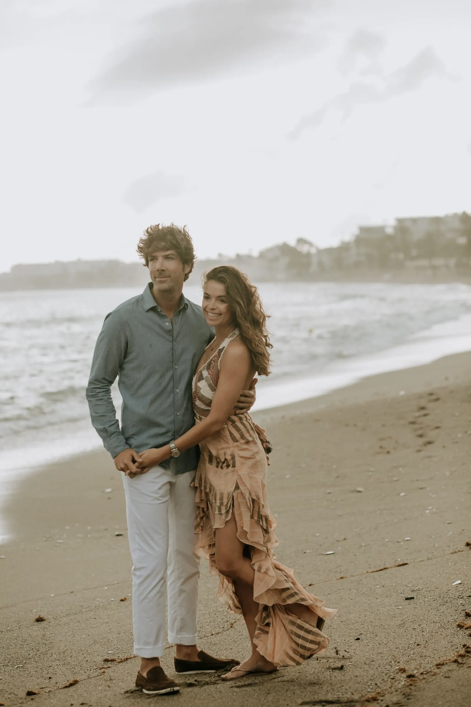 La pareja abrazada en la arena, ella de rosa y él con camisa verde, sesión preboda en la playa, Sotogrande