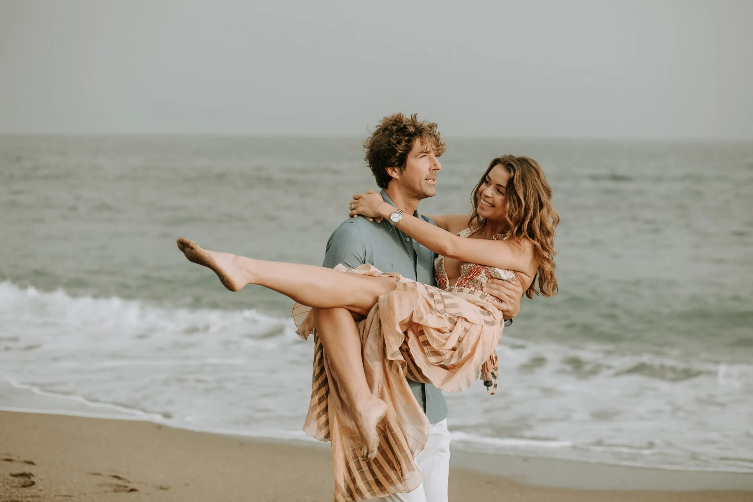 Arnaud levanta a Lauren en brazos en la orilla, sesión preboda en la playa de Sotogrande
