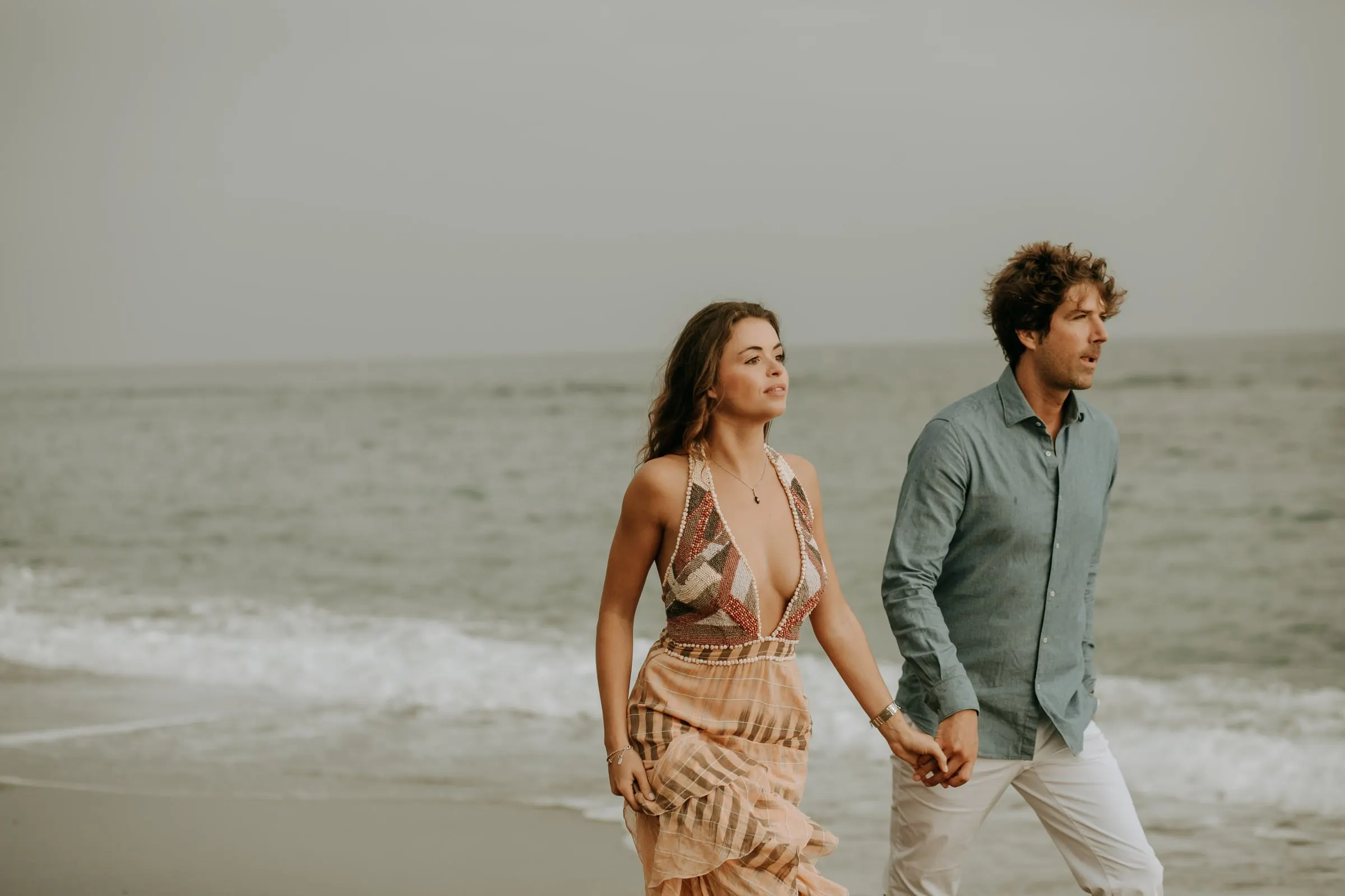 La pareja paseando de la mano por la orilla con las olas detrás, sesión preboda en la playa de Sotogrande